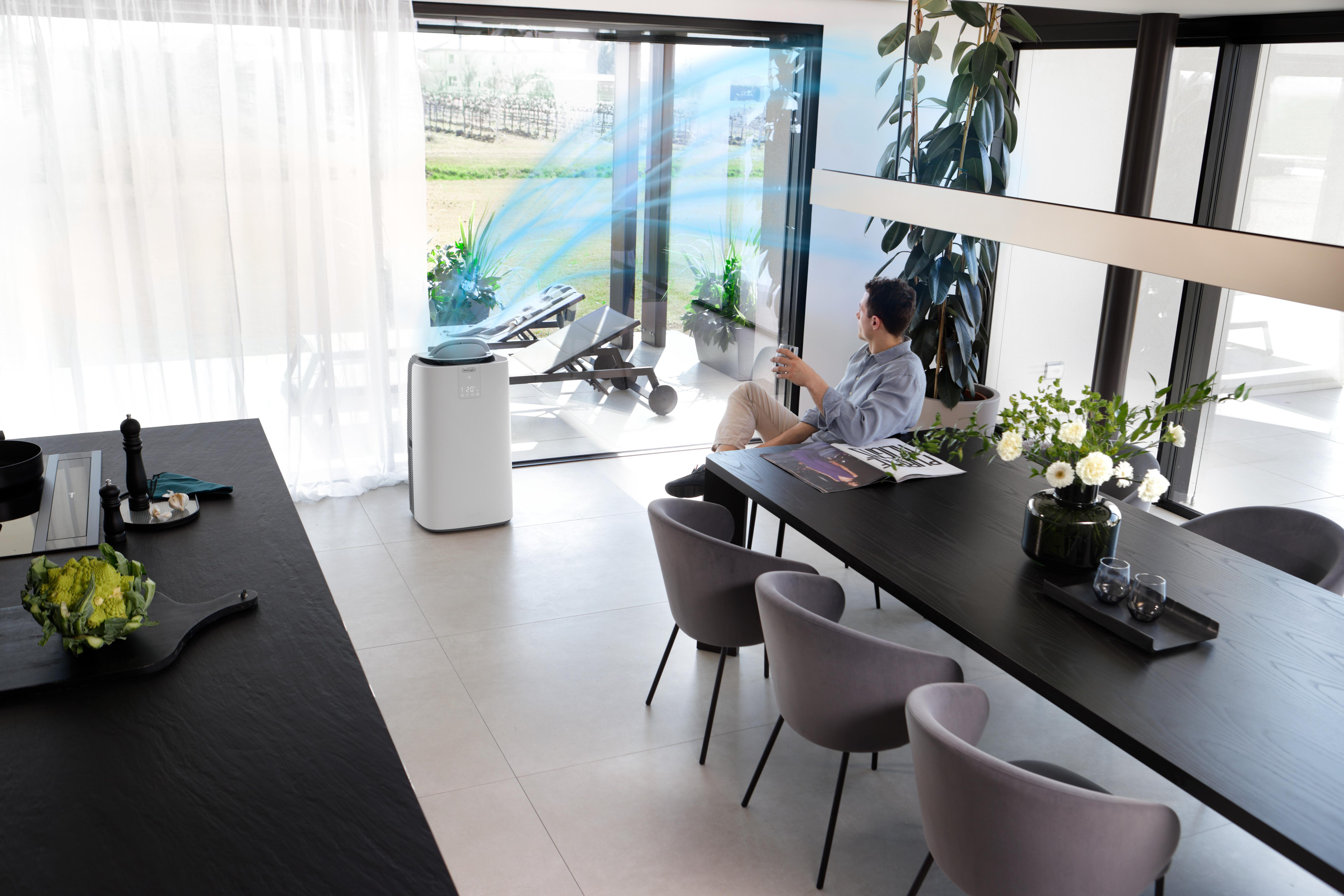 Ein Mann sitzt in einem modernen Esszimmer mit einem Luftreiniger und blauem Luftstrom.