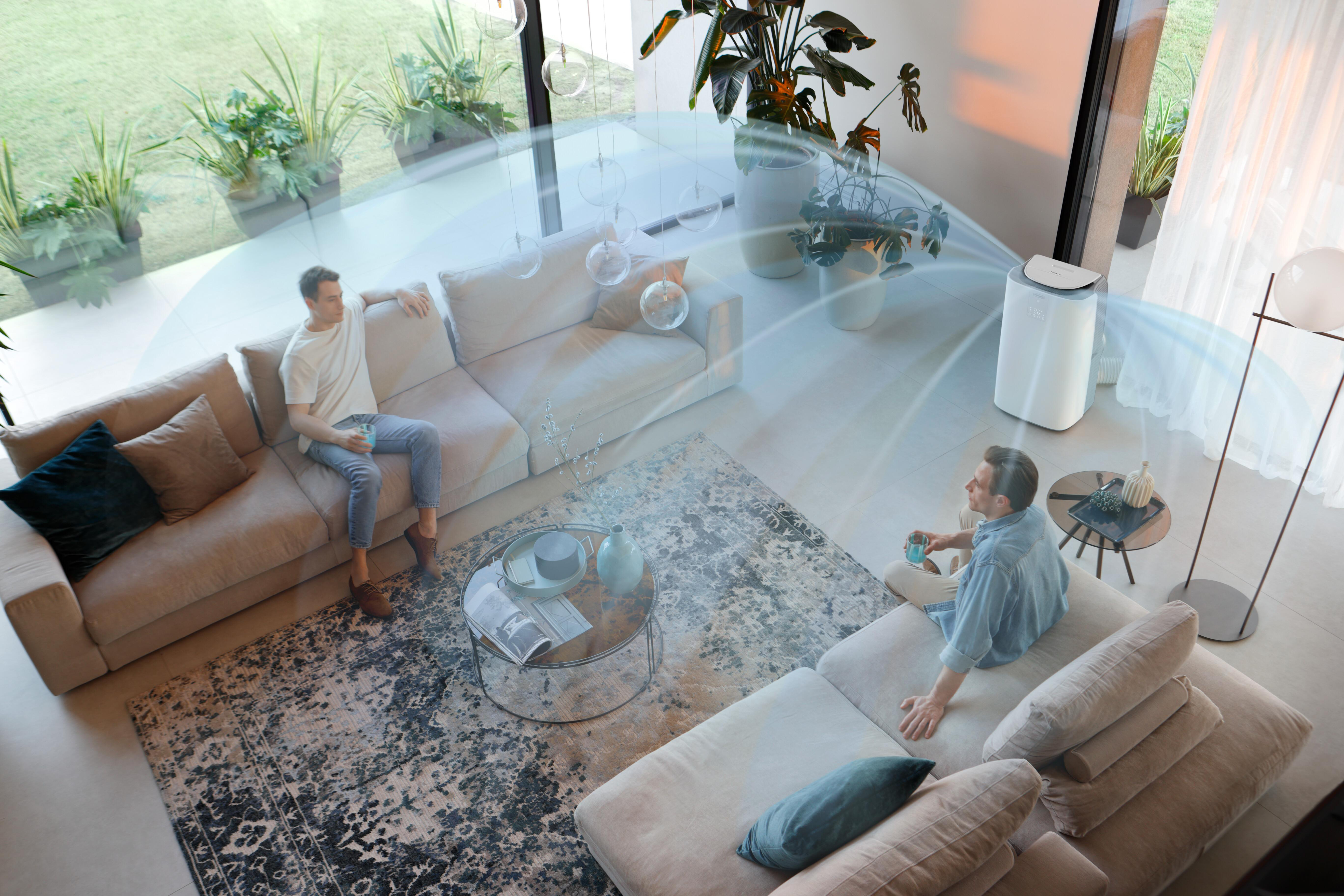 Zwei Männer sitzen auf Sofas in einem modernen Wohnzimmer. Ein Luftreiniger ist in Betrieb.