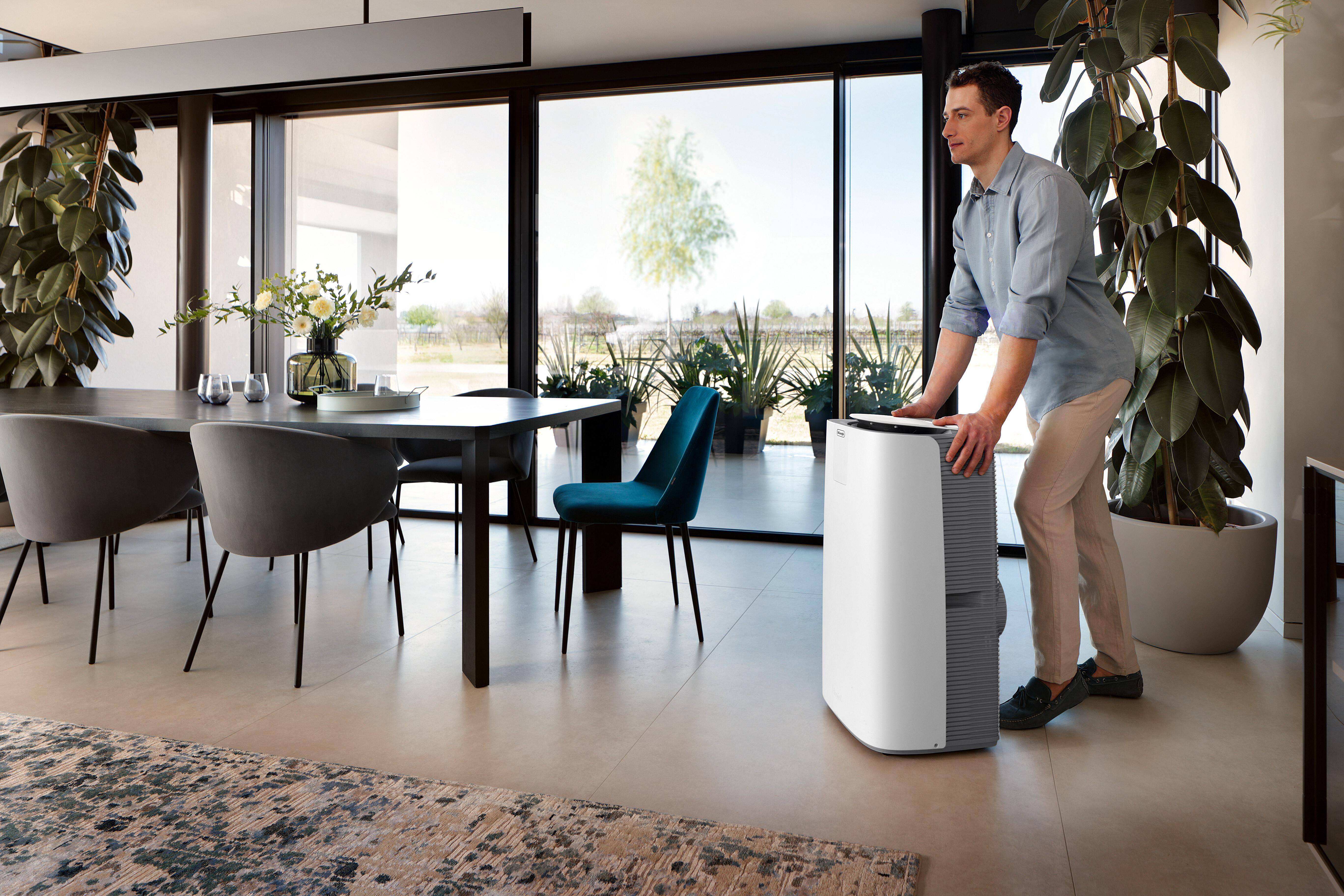 Mann bedient Luftreiniger im modernen Esszimmer mit großen Fenstern.
