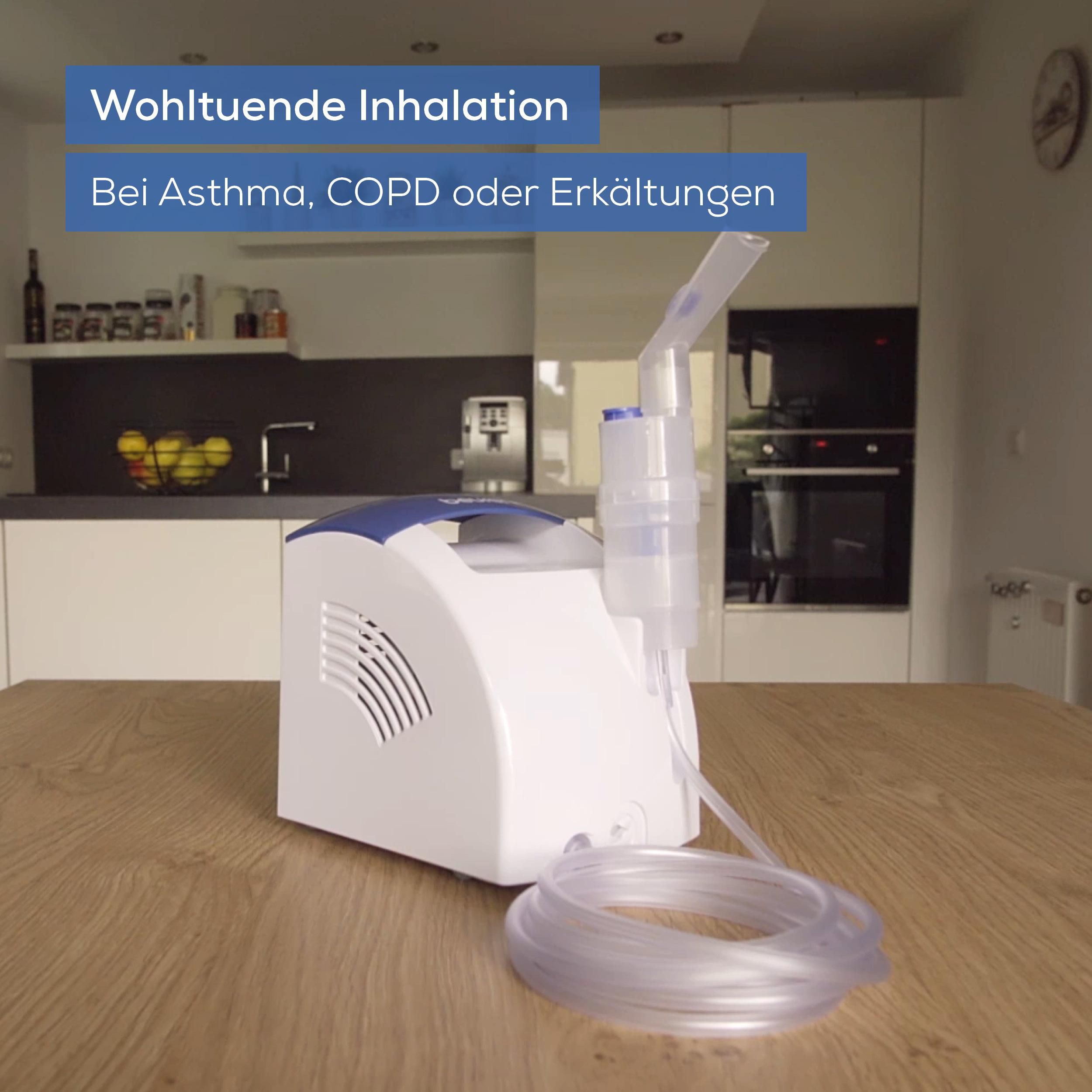 Ein weißer Inhalator mit blauem Deckel steht auf einem Holztisch. Ein Schlauch liegt daneben.