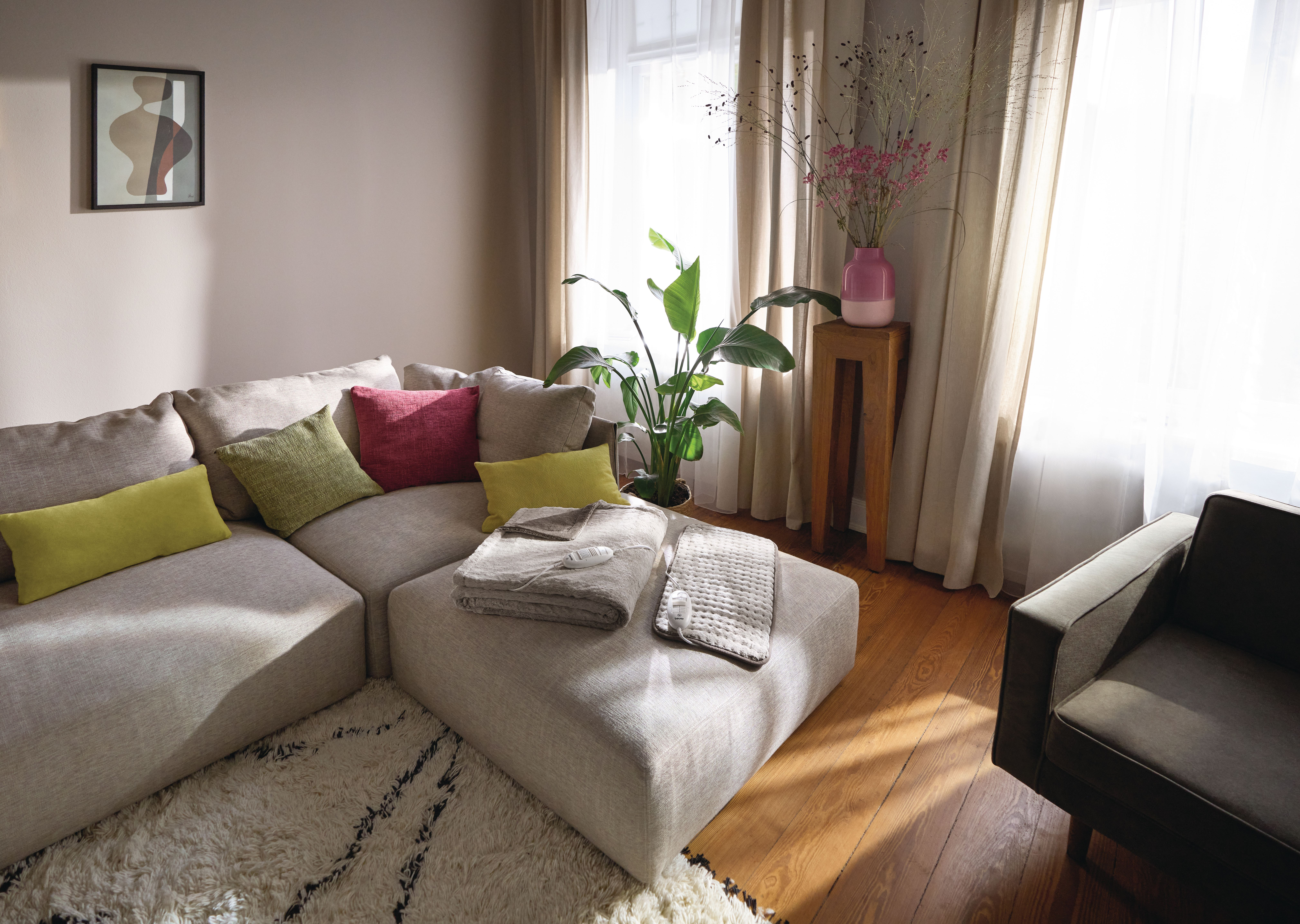 Ein beiger Ecksofa mit Kissen und Decken, daneben ein Sessel.