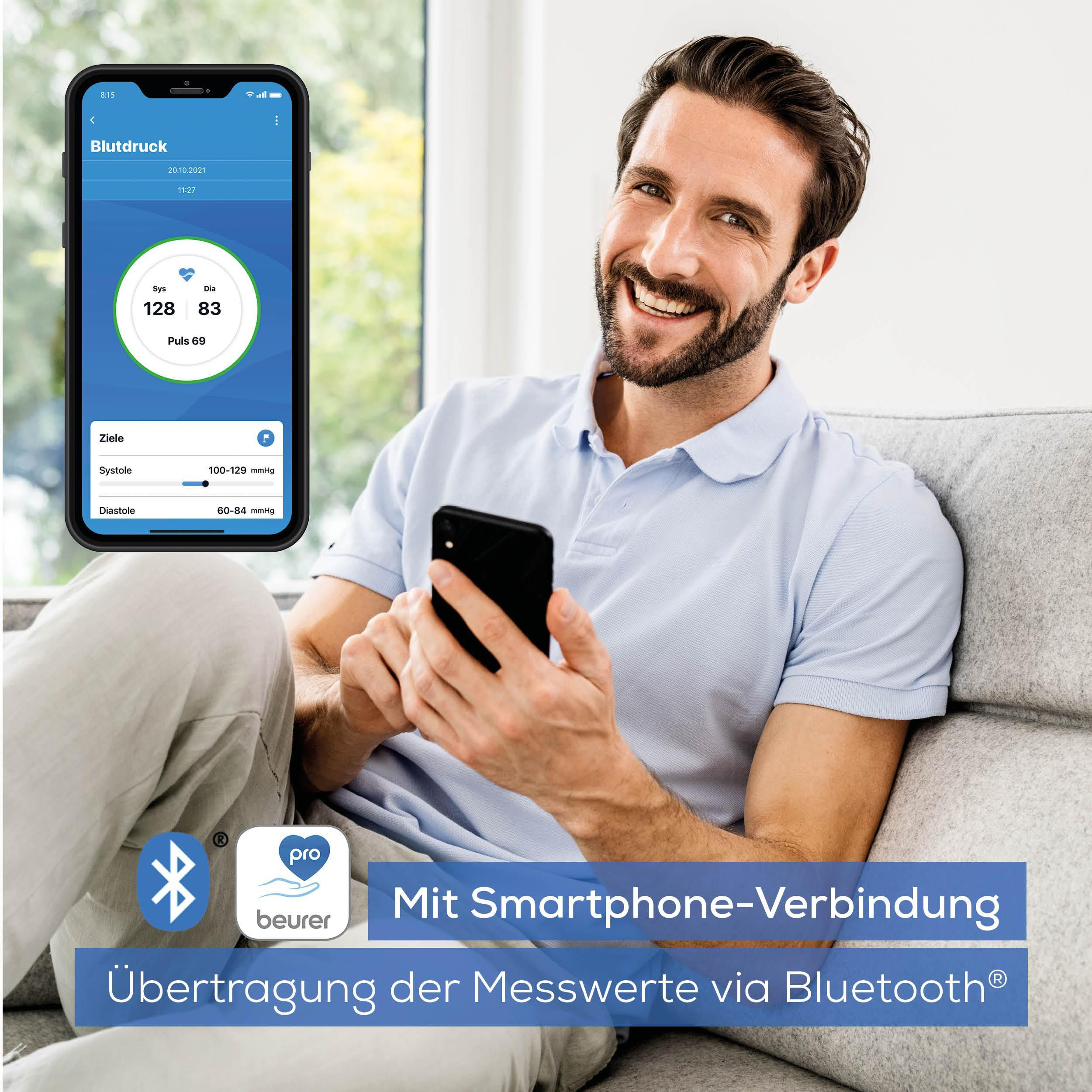 Mann sitzt auf Sofa mit Handy, das Blutdruckwerte anzeigt.