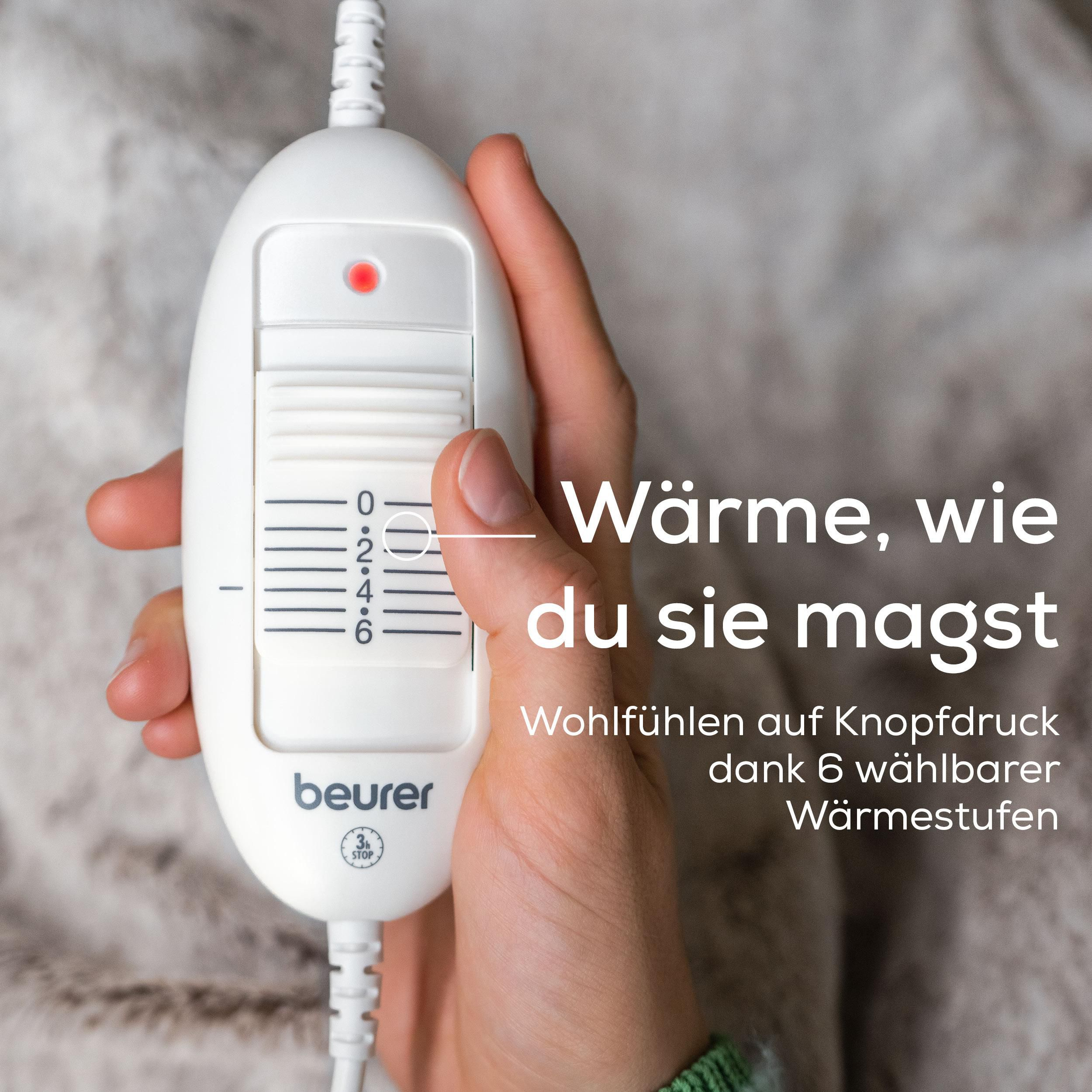 Hand hält ein weißes Heizkissen-Bedienteil mit Skala von 0-6.