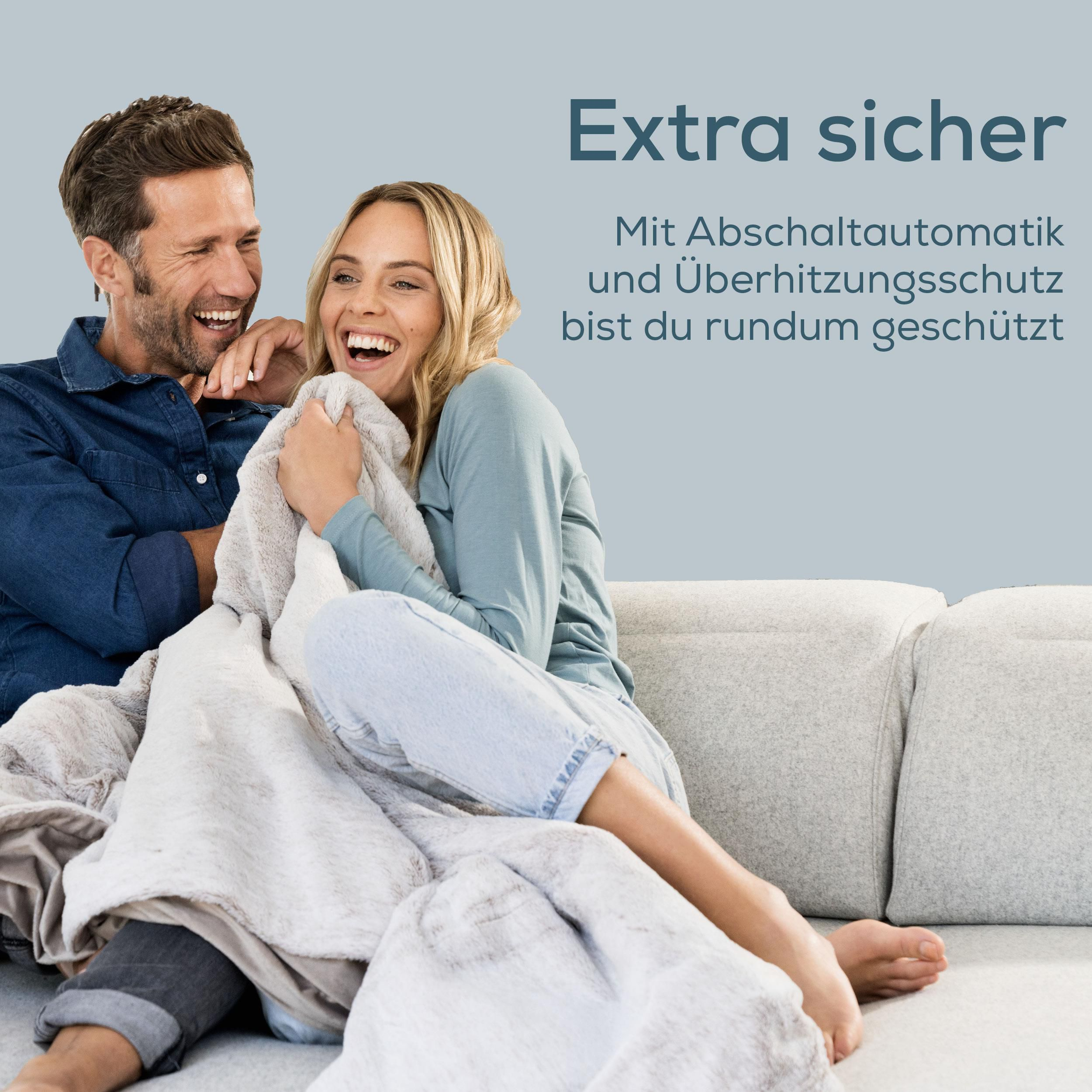 Ein lachendes Paar auf einem Sofa, mit einer Decke bedeckt.