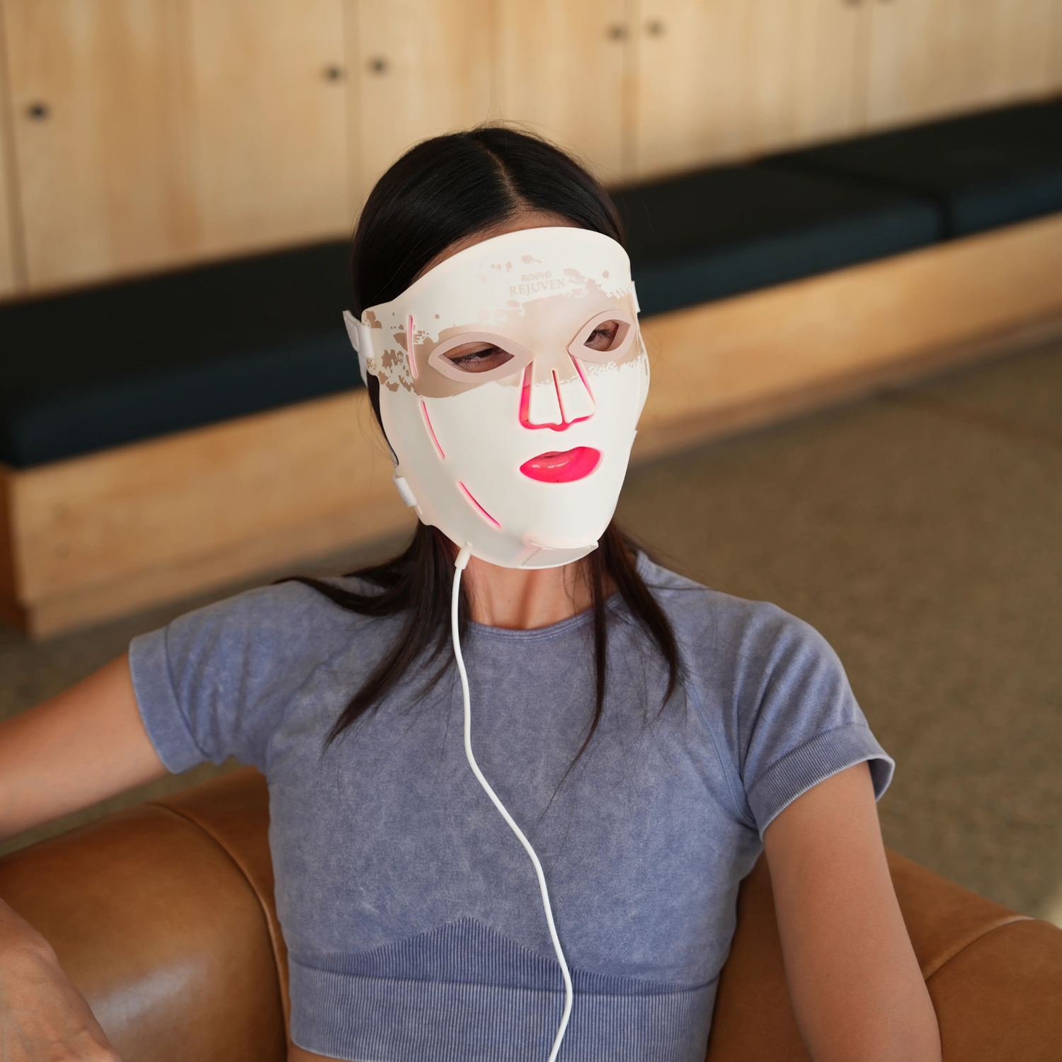 Woman wearing a face mask sits on a brown leather sofa.