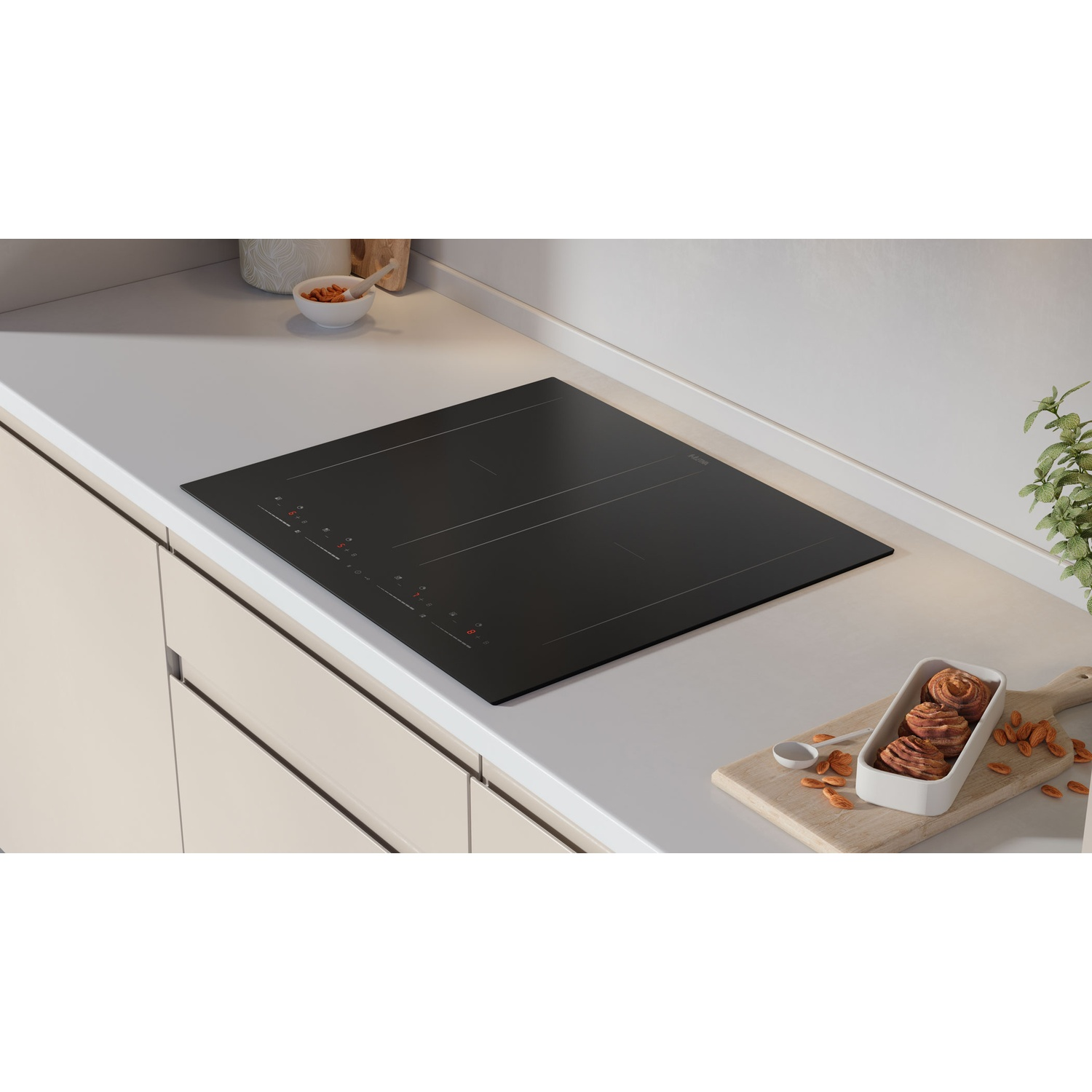 A black induction hob on a light countertop with a dish of sweets and almonds beside it.