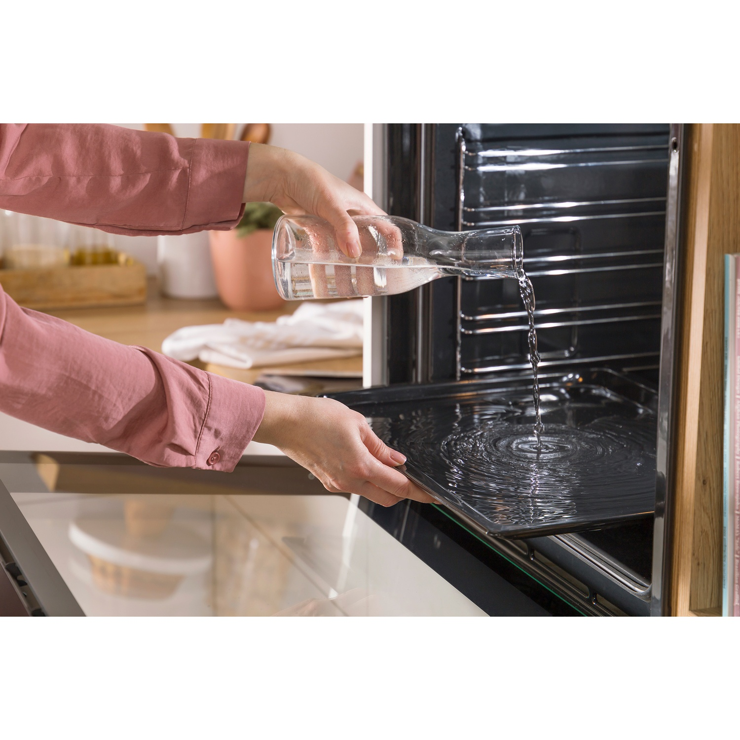 Een persoon giet water uit een karaf op een bakplaat in een oven.