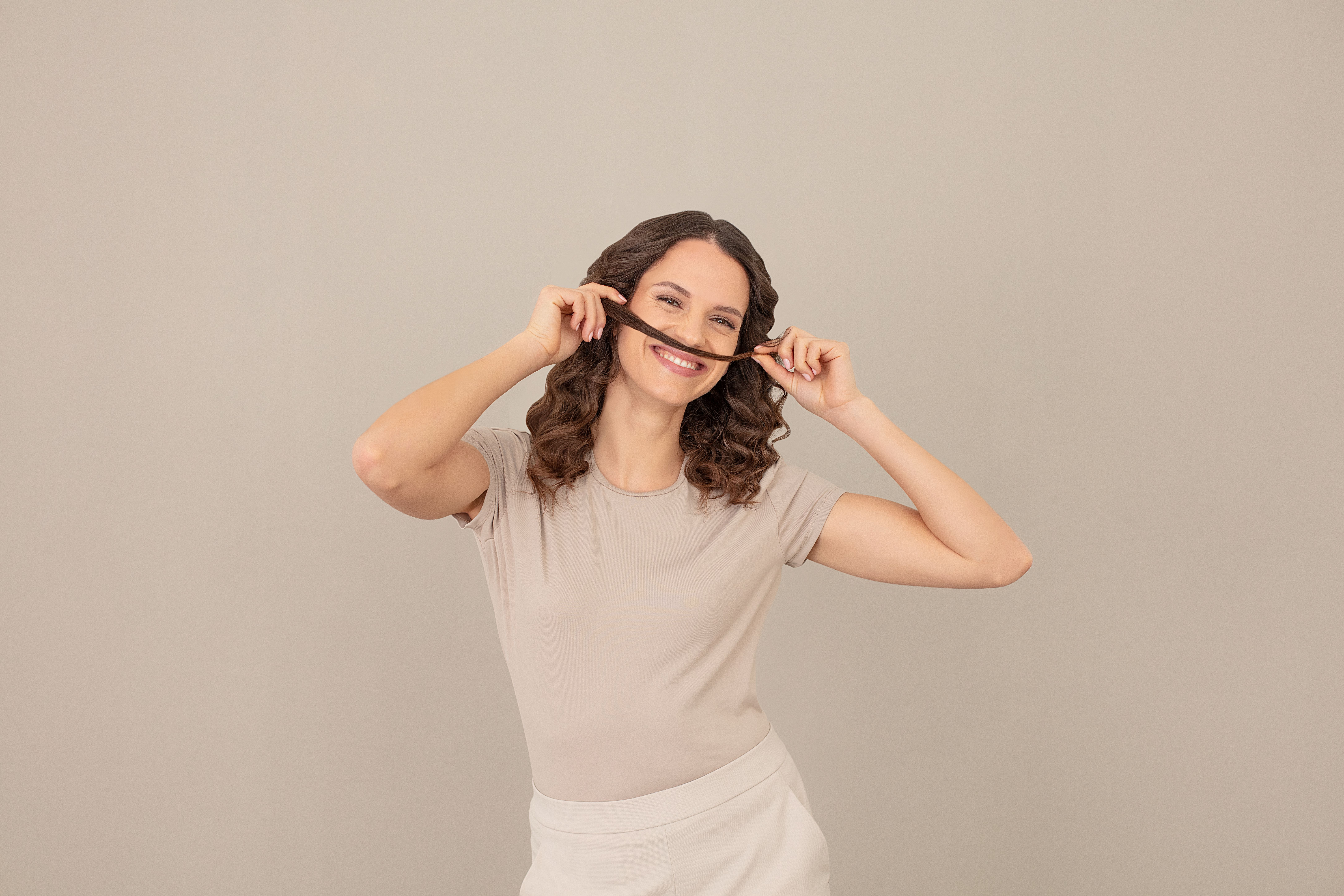 Eine Frau mit braunem Haar hält eine Haarsträhne über ihre Oberlippe.