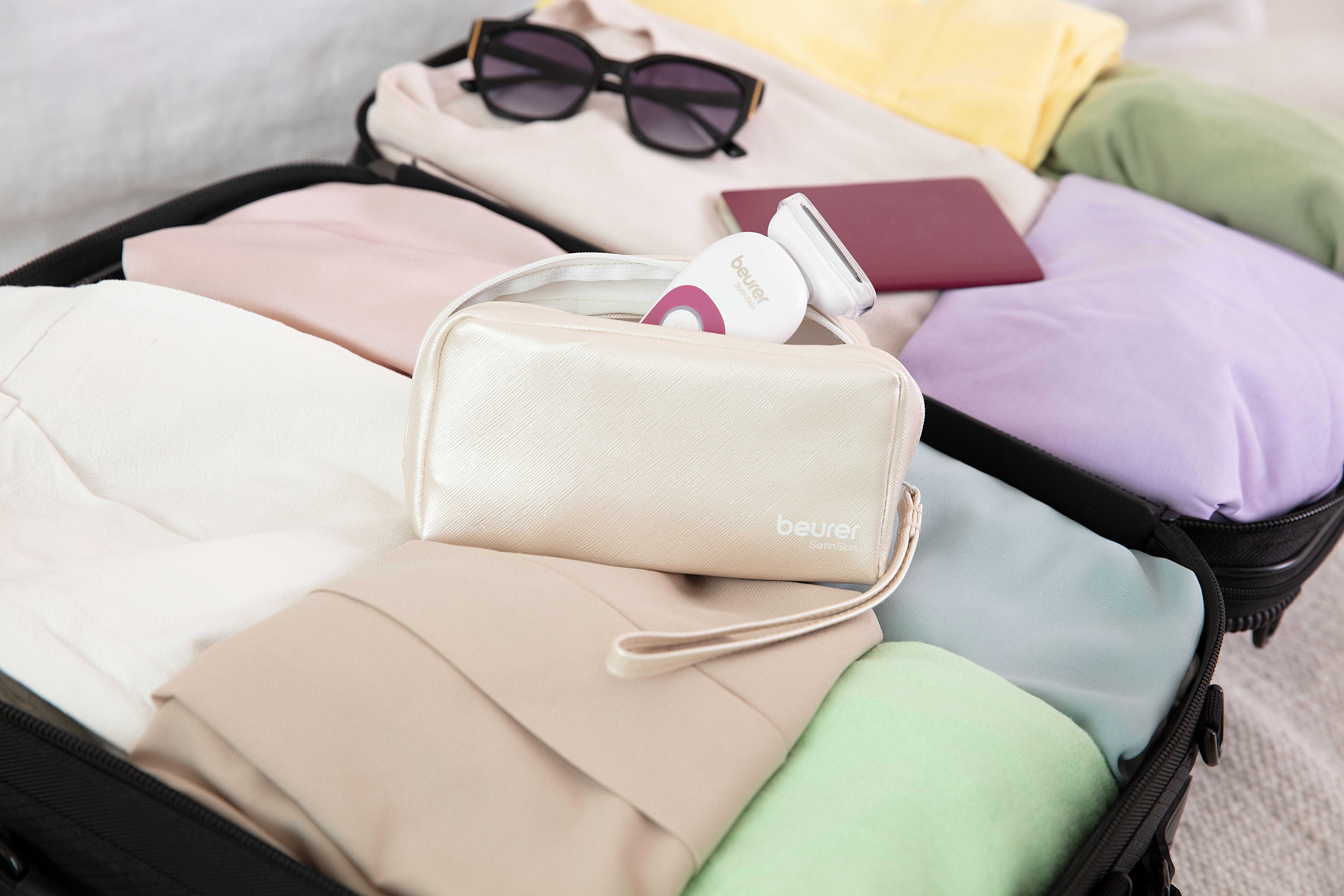 Ein offener Koffer mit Kleidung in Pastellfarben, Sonnenbrille und Kosmetiktasche.