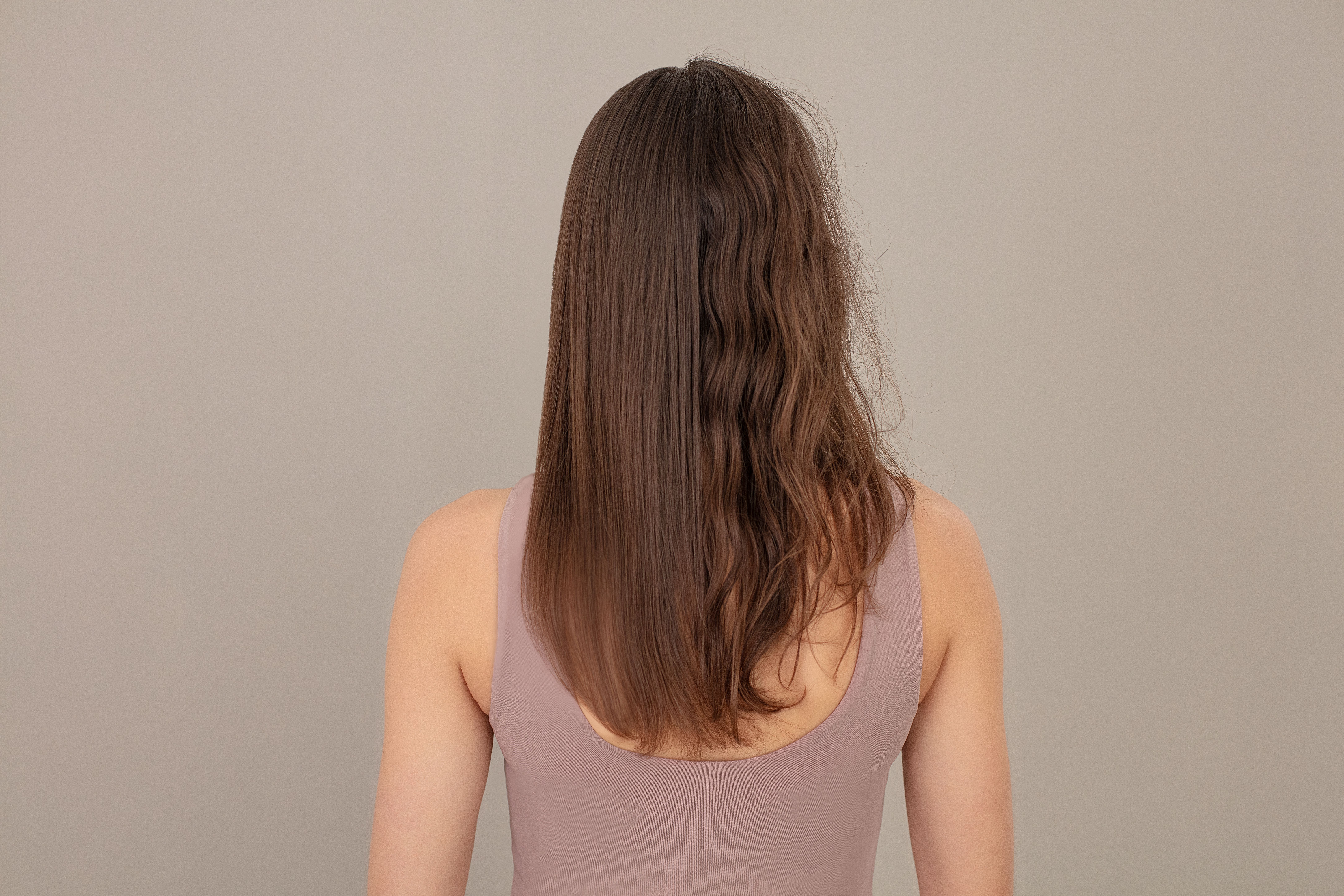 Rückansicht einer Frau mit langen braunen Haaren, die linke Seite ist glatt, die rechte ist wellig.