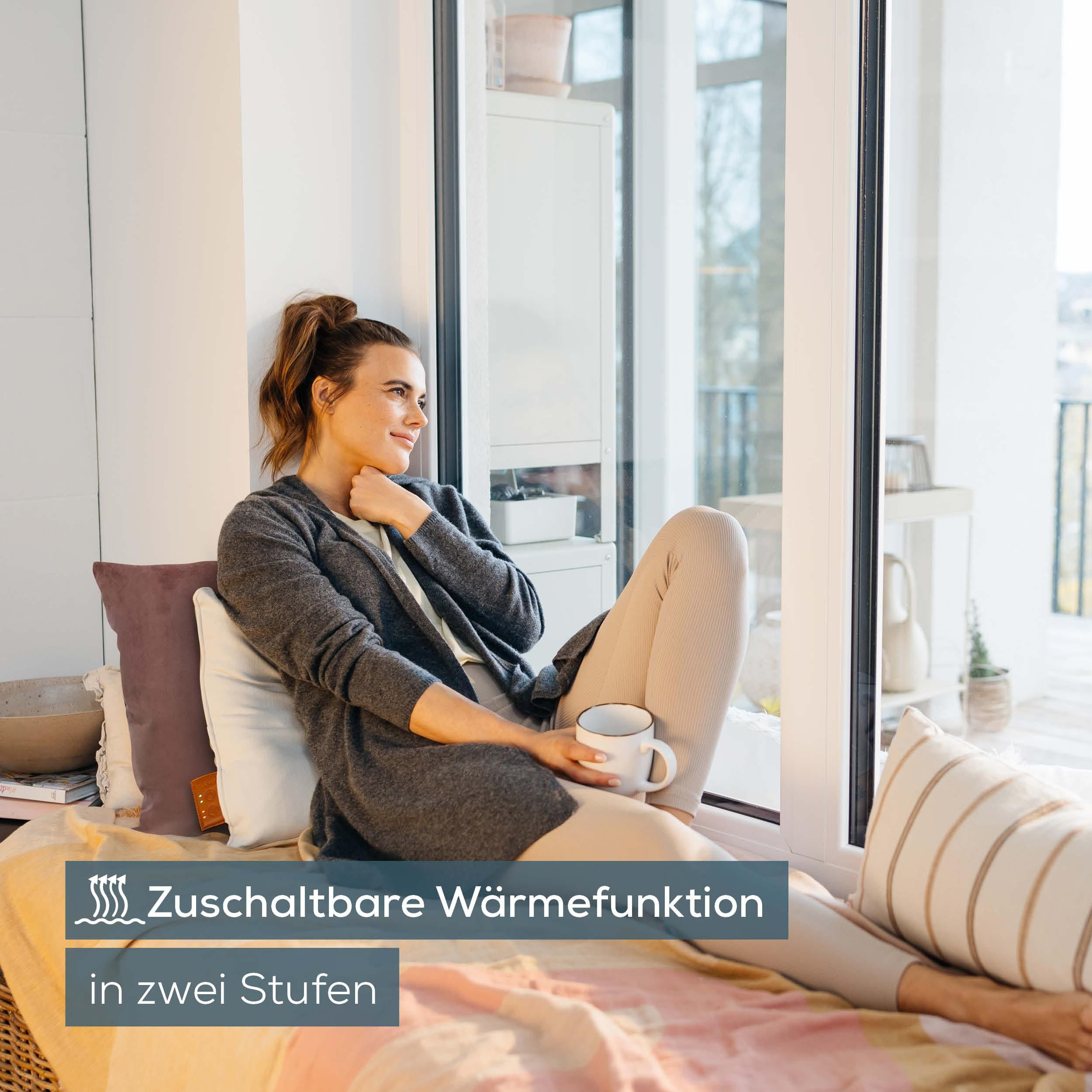 Eine Frau sitzt auf einem Fensterplatz und hält eine Tasse. Text über Wärme.