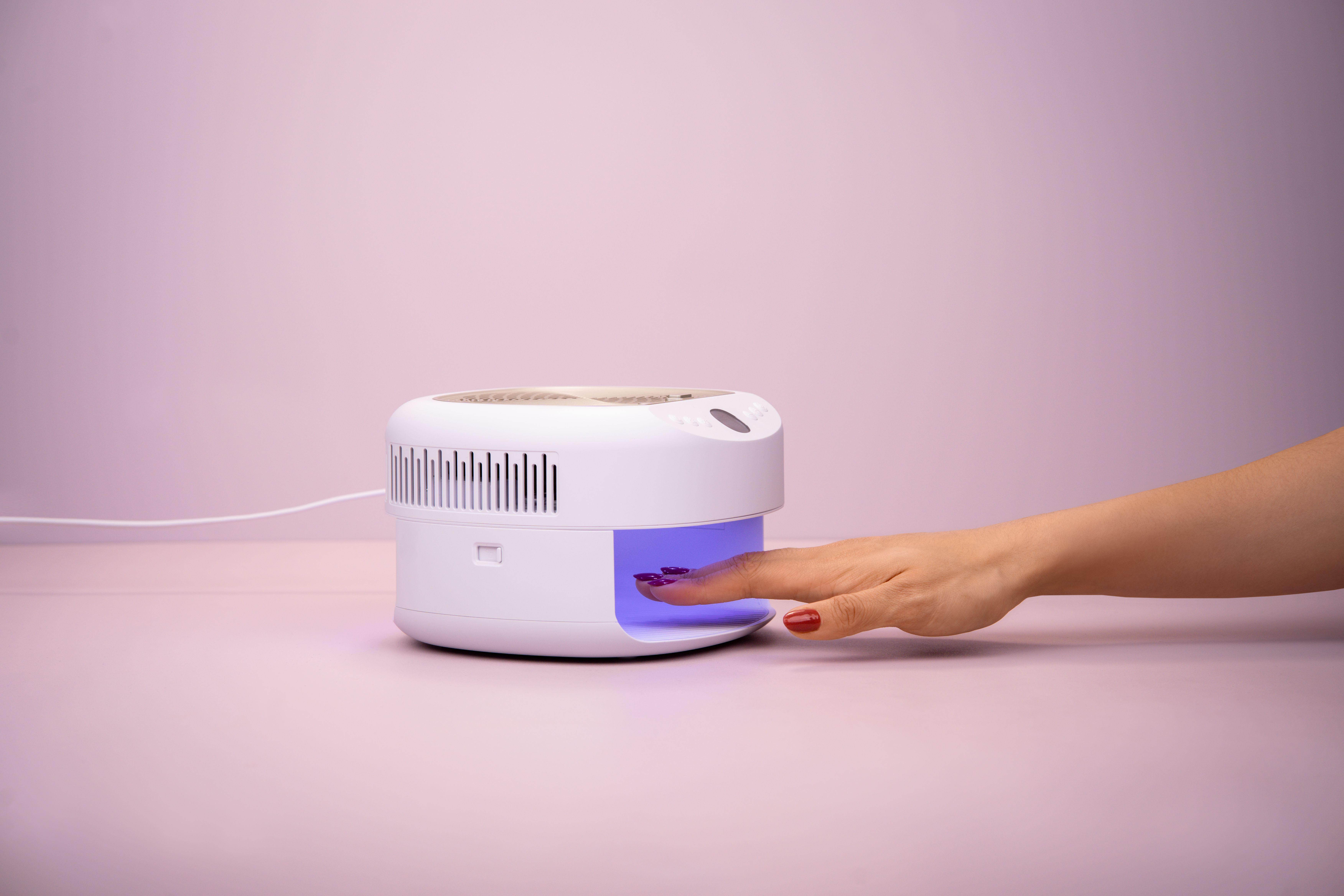 Eine Hand mit lila Nagellack trocknet unter einer weißen UV-Lampe.