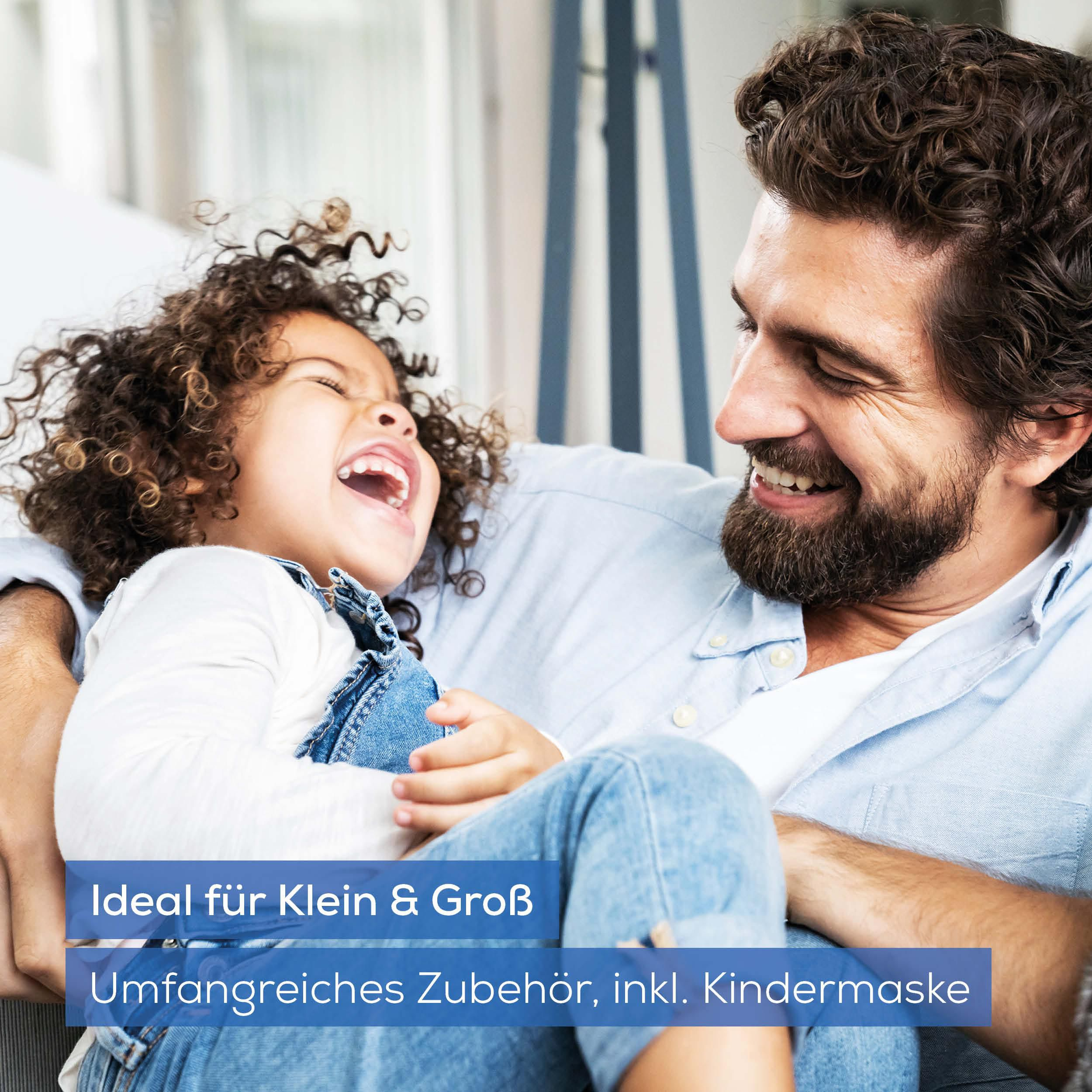 Vater und Kind lachen, beide in Jeanskleidung, drinnen.