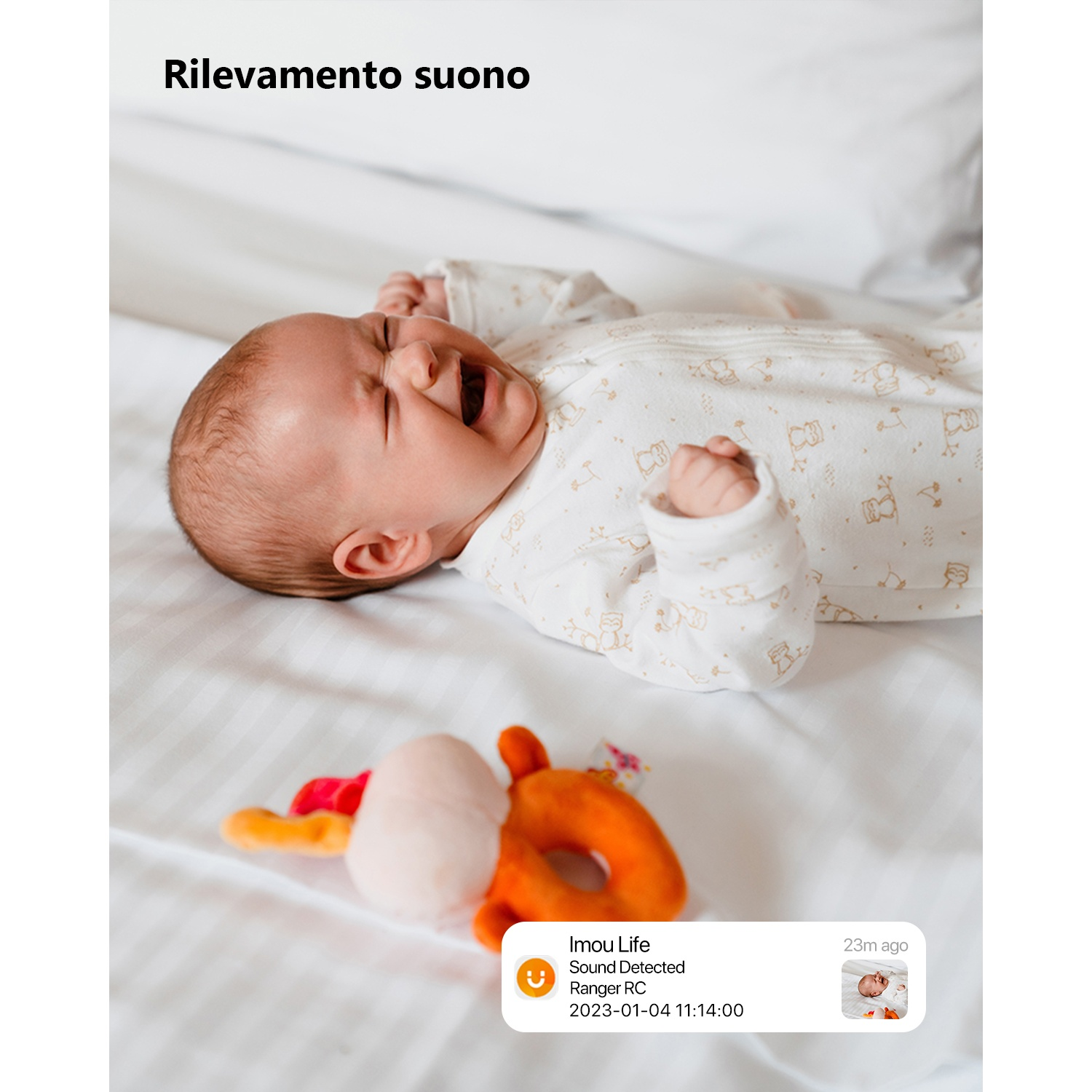 Un bambino che piange giace sul letto con un giocattolo vicino.