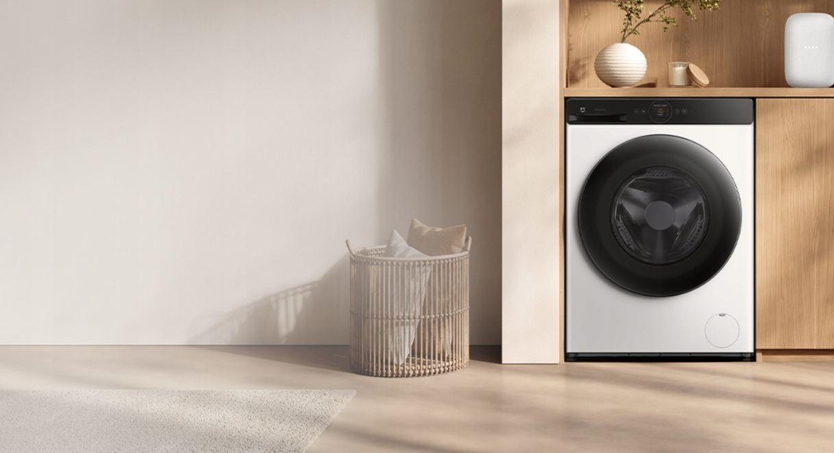 Biała pralka z czarnymi drzwiami stoi obok drewnianej szafki. Po lewej znajduje się kosz na pranie.