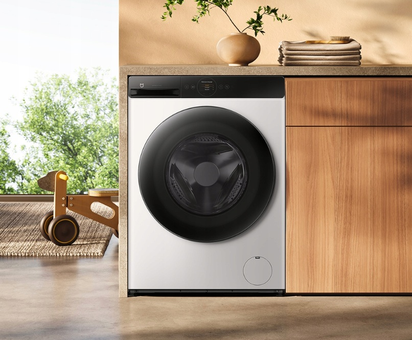 Biała pralka z czarnymi drzwiami stoi obok drewnianych szafek.