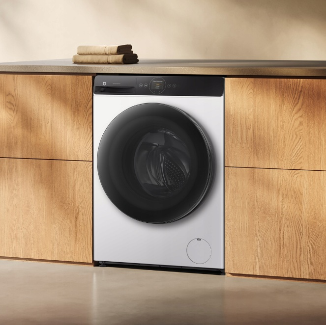 Biała pralka z czarnymi drzwiami stoi między drewnianymi szafkami.