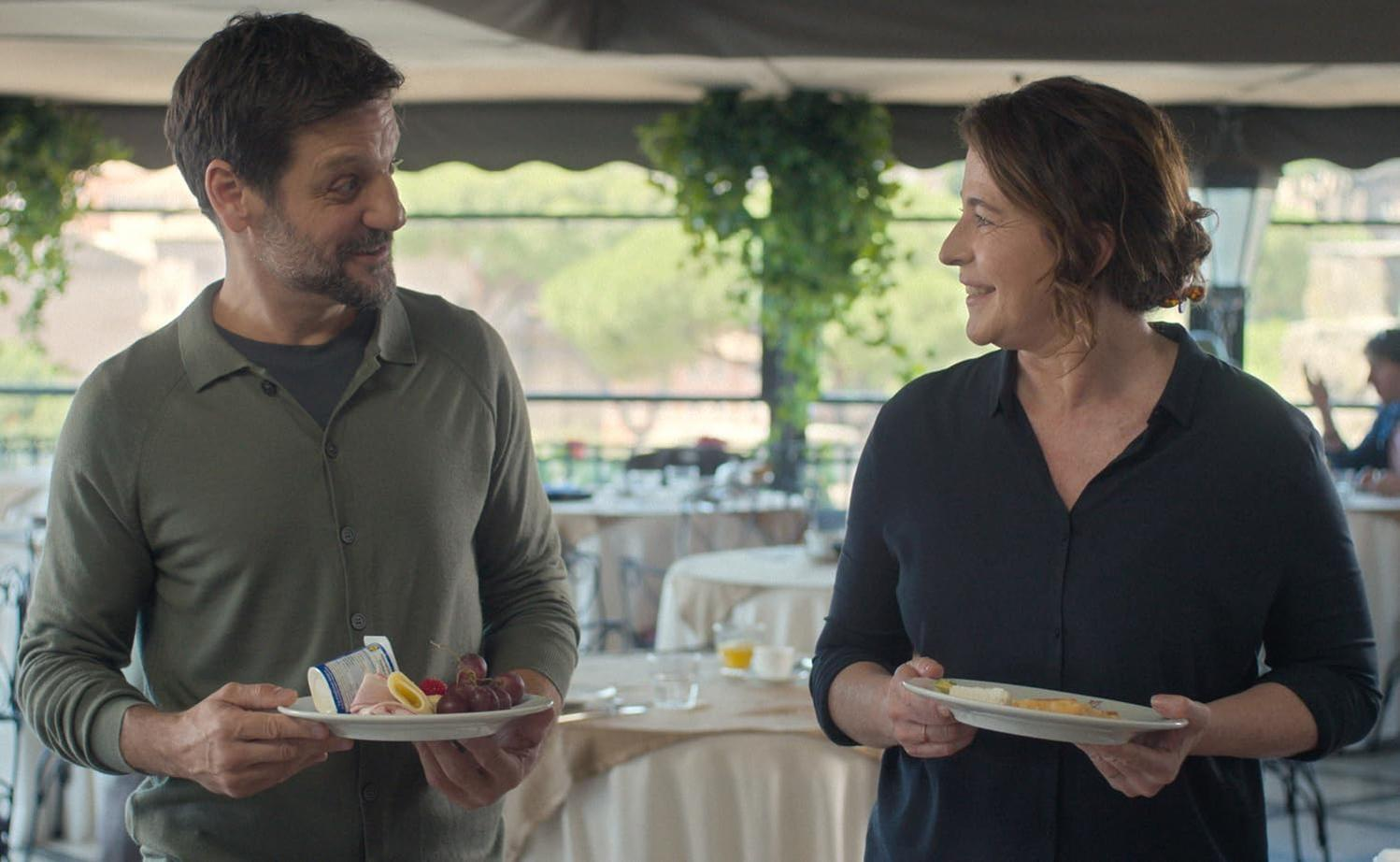 Mann und Frau stehen mit Tellern voller Essen und unterhalten sich.
