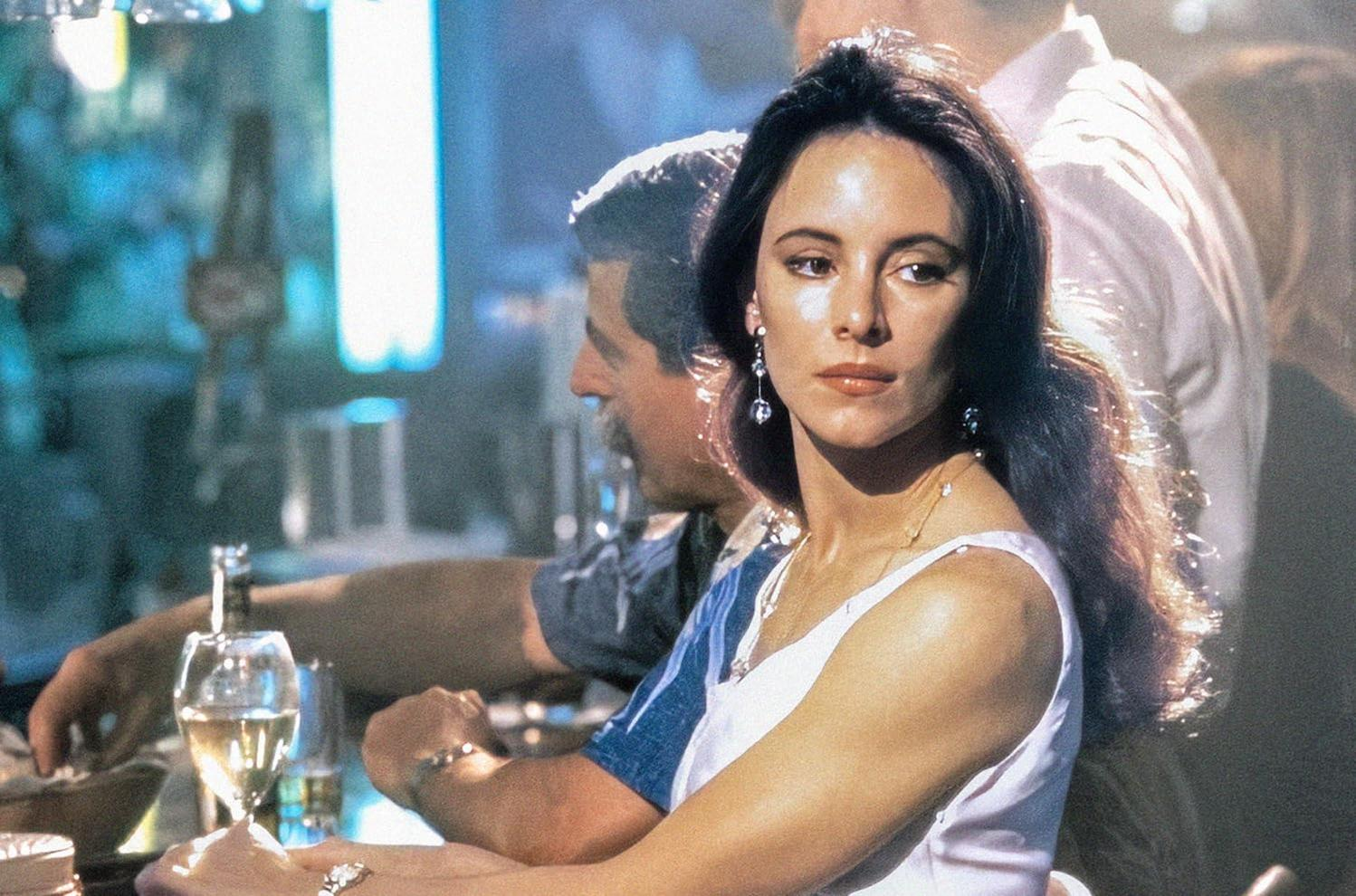 Eine Frau mit dunklen Haaren sitzt an einer Bar mit einem Glas Wein.