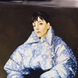 Eine Frau mit kurzen schwarzen Haaren trägt eine blaue Pufferjacke mit weißen Tupfen.