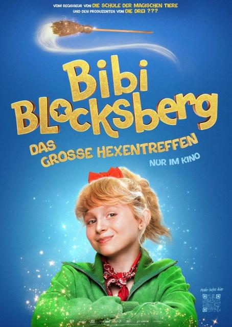 Ein Mädchen mit roten Schleifen im blonden Haar, grüne Jacke, vor blauem Himmel.