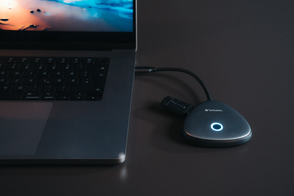 Egy szürke laptop egy kék fényű fekete USB-elosztóhoz csatlakozik.