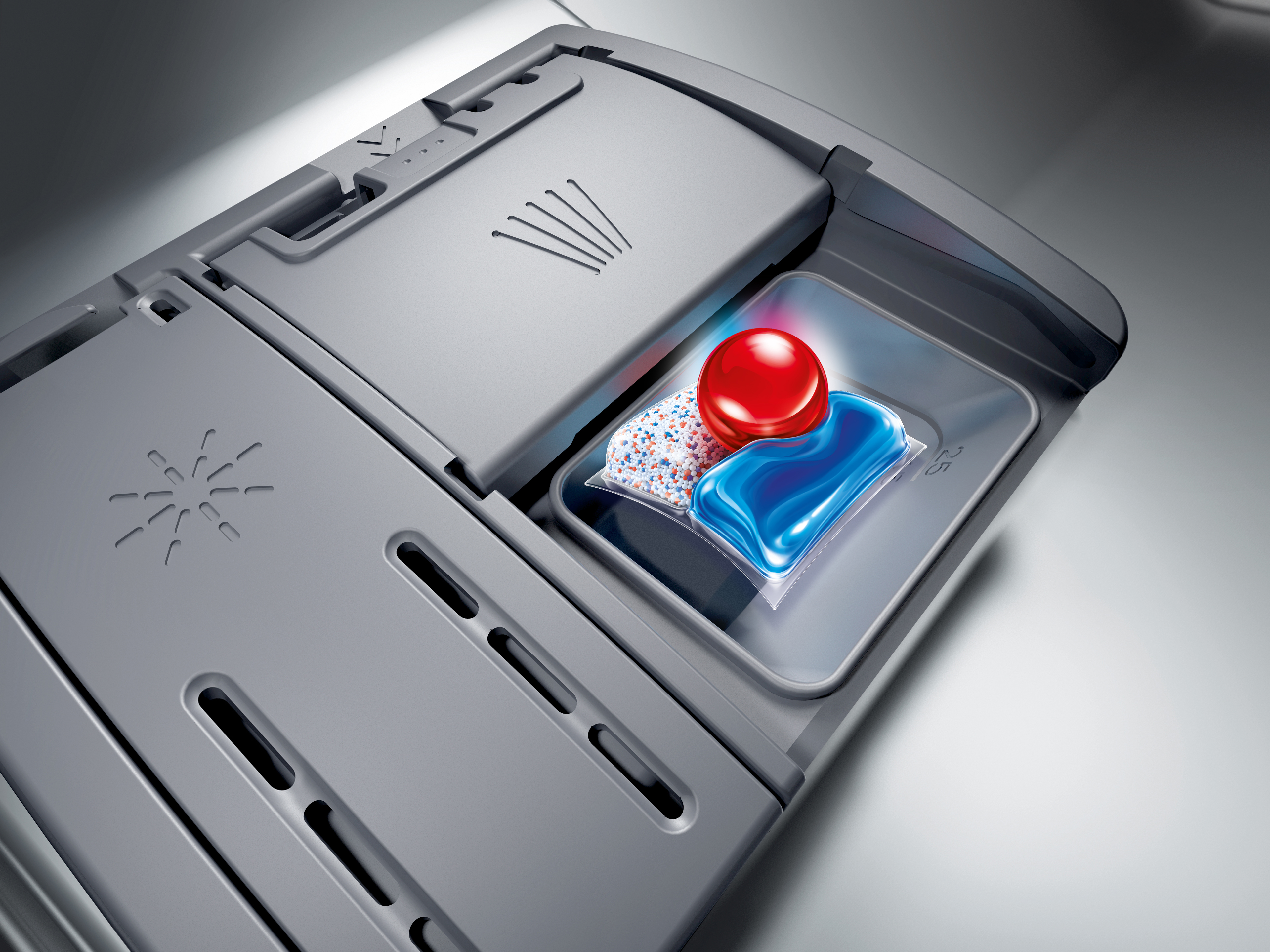 Capsula per lavastoviglie con gel blu, polvere e sfera rossa in un vano.