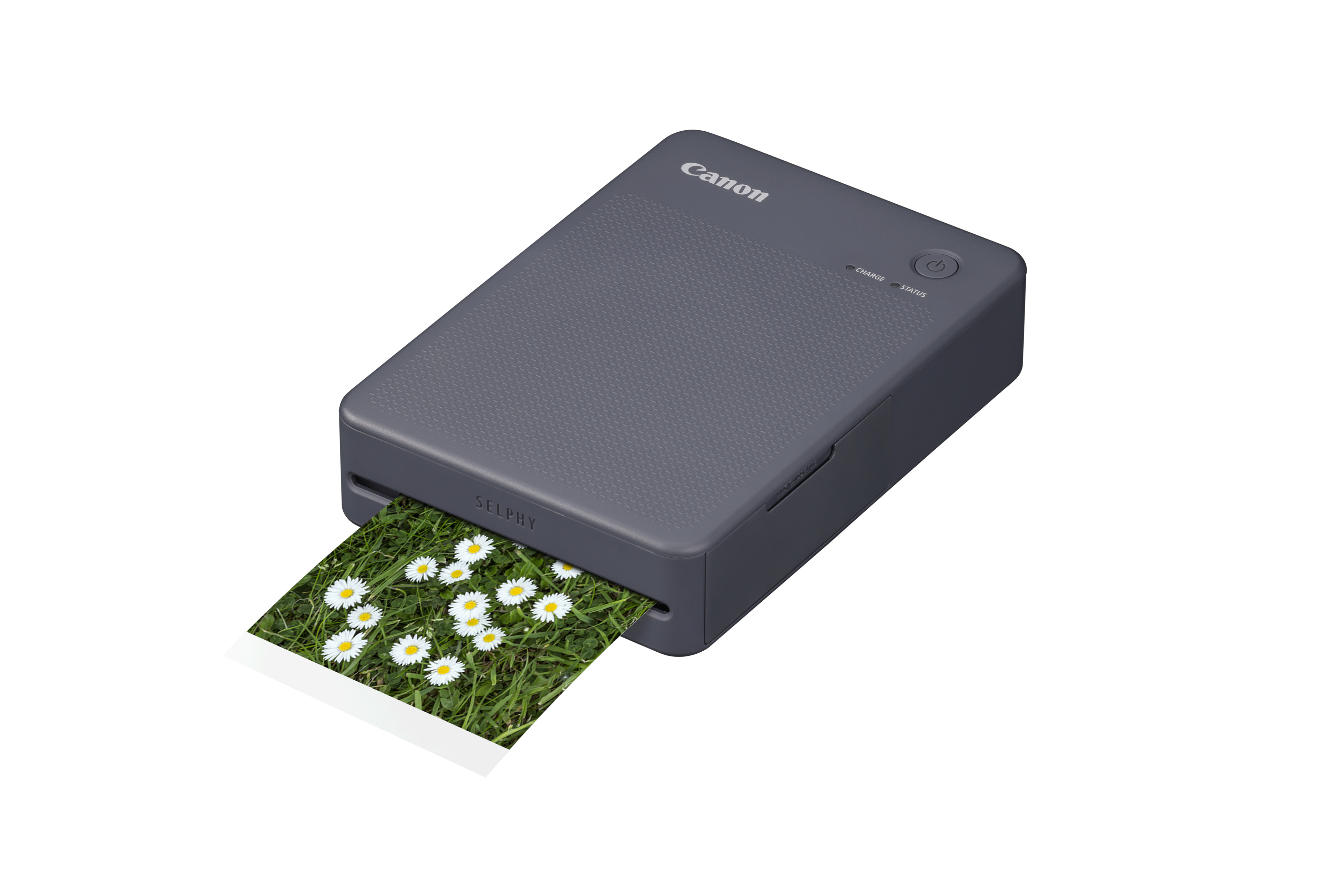 Szara drukarka Canon Selphy drukuje zdjęcie stokrotek na zielonej trawie.