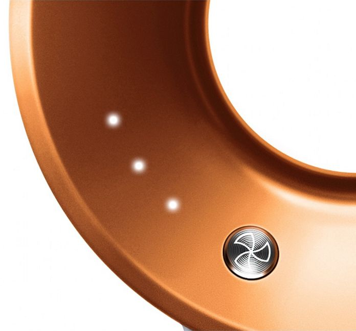 Gros plan d'un appareil incurvé de couleur bronze avec trois petites lumières vives et un bouton circulaire avec une icône de ventilateur.