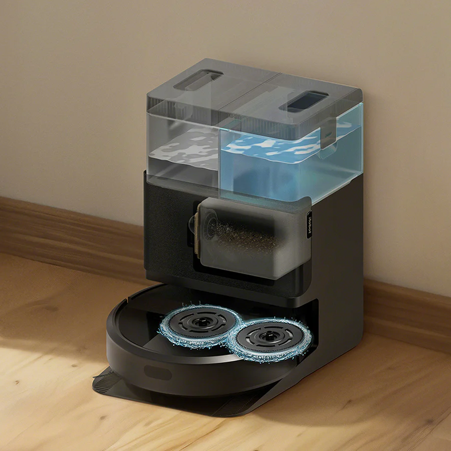 Eine schwarze Roboter-Staubsaugerbasis mit zwei durchsichtigen Wassertanks, einer voll mit sauberem blauem Wasser, auf einem Holzfußboden.