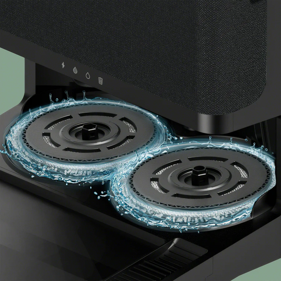 Nahaufnahme einer schwarzen Roboterstaubsaugerbasis mit zwei sich drehenden runden Wischpads, umgeben von spritzendem Wasser.