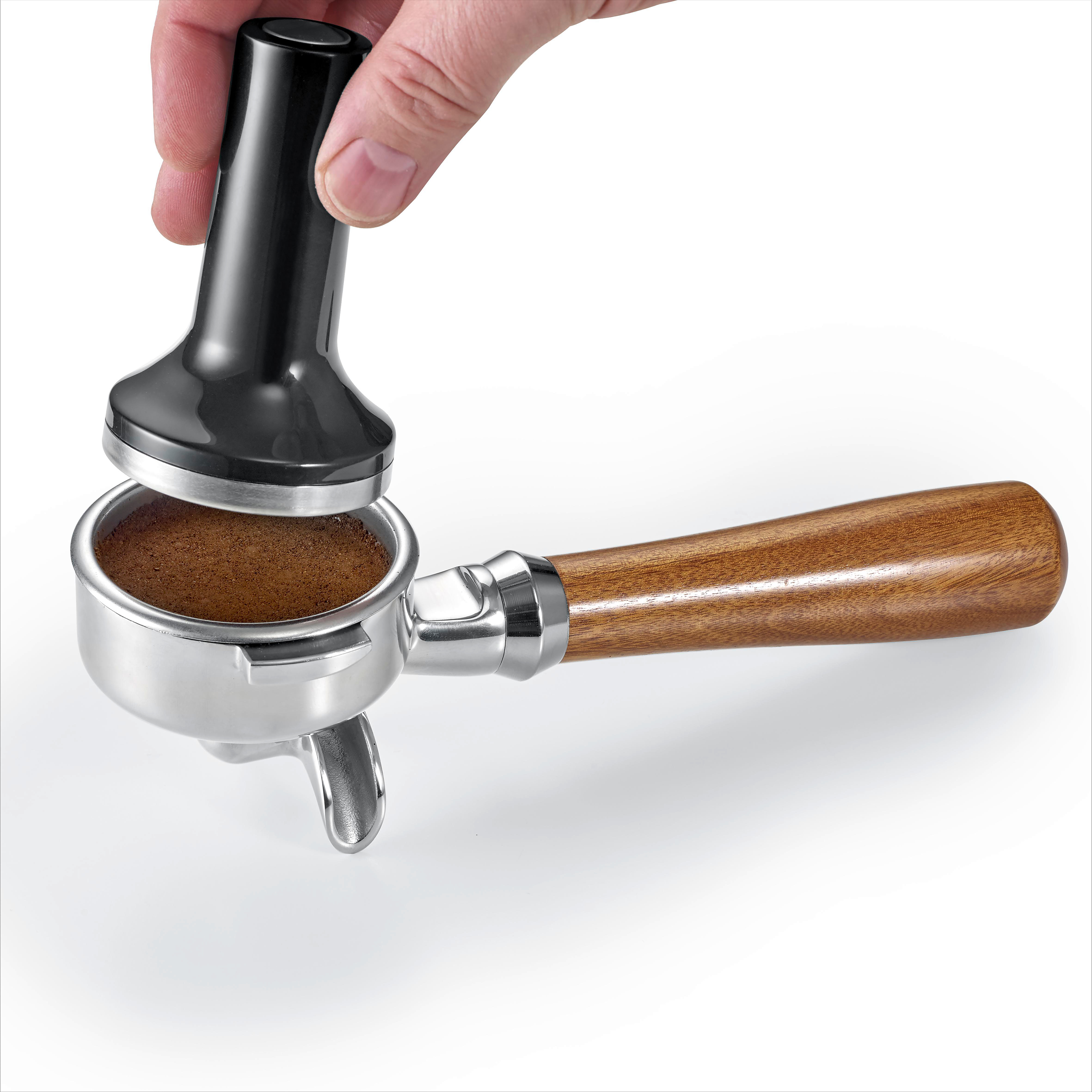 Eine Hand hält einen schwarzen Tamper über einem Siebträger mit Kaffeepulver.