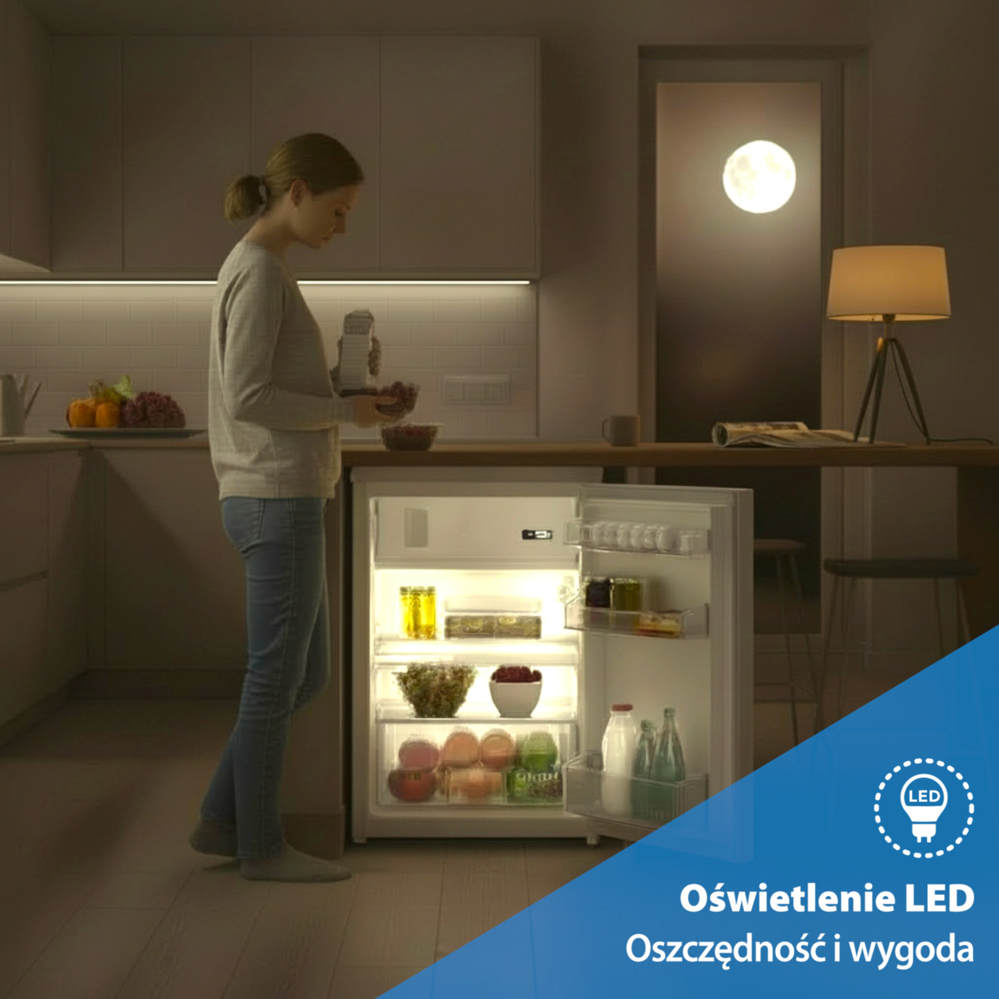 Kobieta w ubraniu wierzchnim otwiera oświetloną lodówkę z jedzeniem.