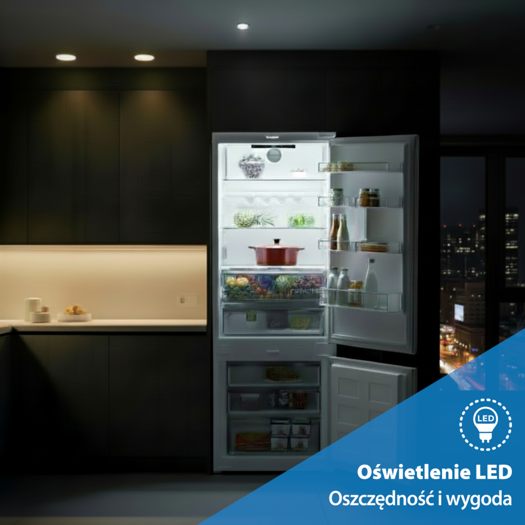 Otwarta lodówka w ciemnej kuchni, oświetlona LED, z widokiem na miasto.