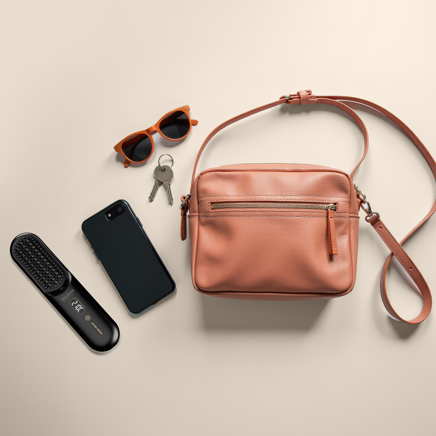Salmon-colored bag, phone, orange sunglasses, keys, and a hair straightener on a light surface.