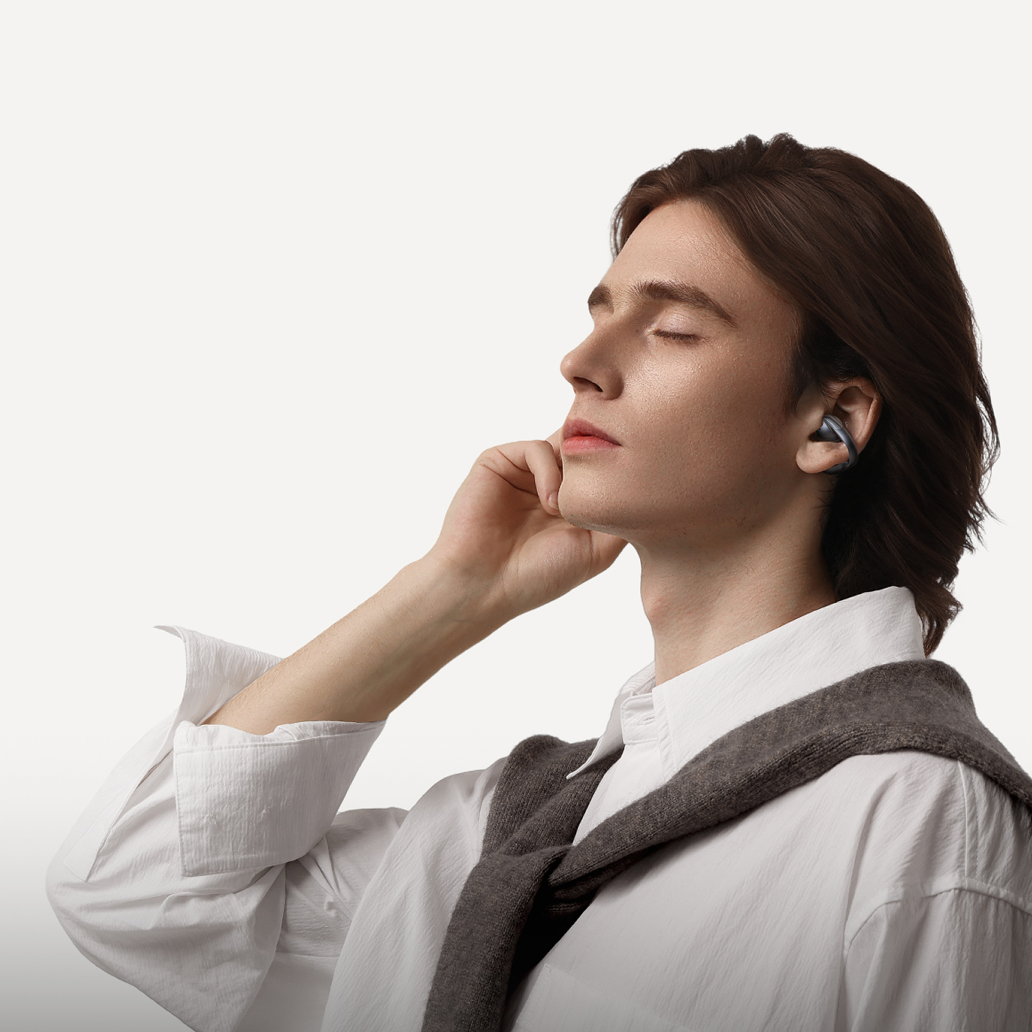 Hombre con ojos cerrados y auriculares, mano en la barbilla, camisa blanca.