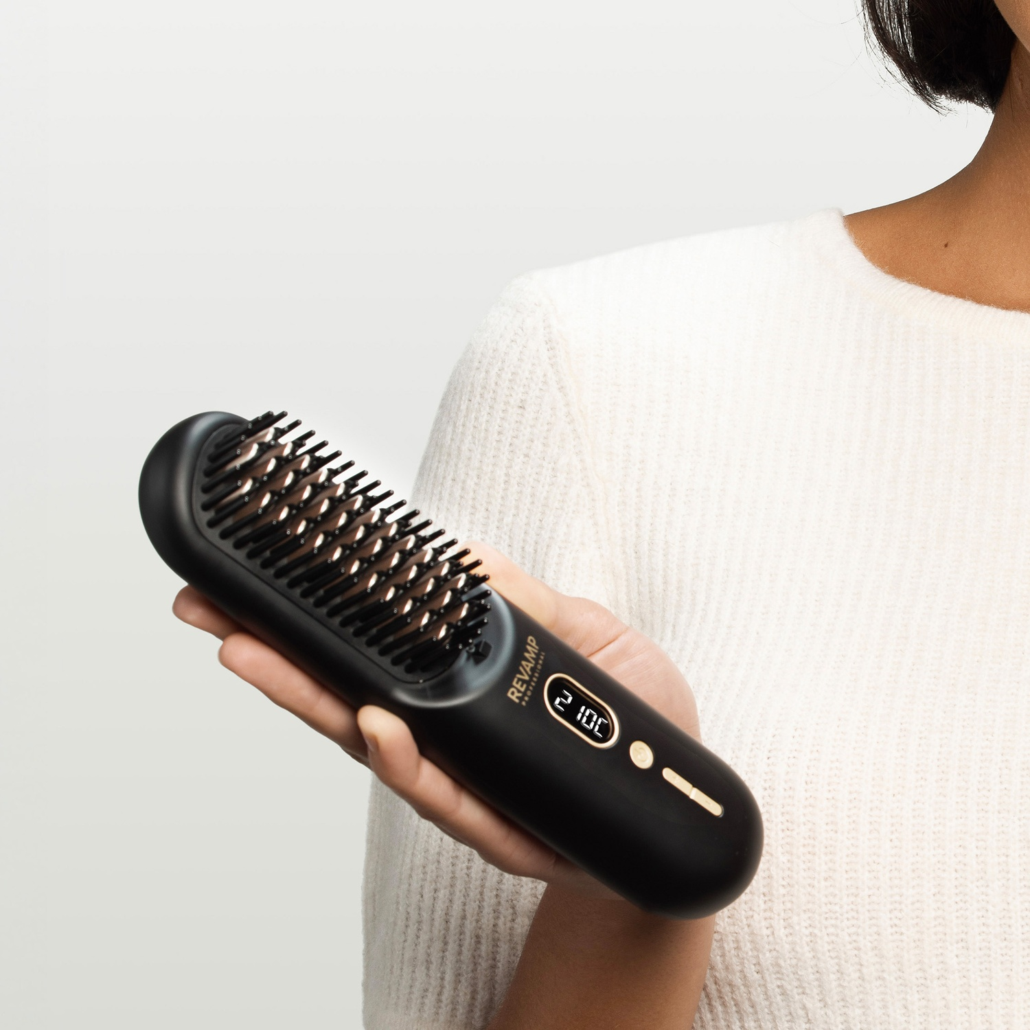 A person holds a black straightening brush with digital settings.