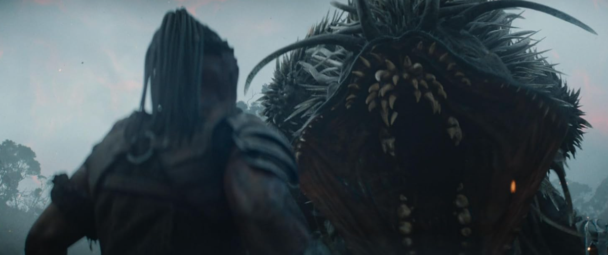 Ein Krieger mit Dreadlocks steht einem riesigen Monster mit spitzen Zähnen gegenüber.