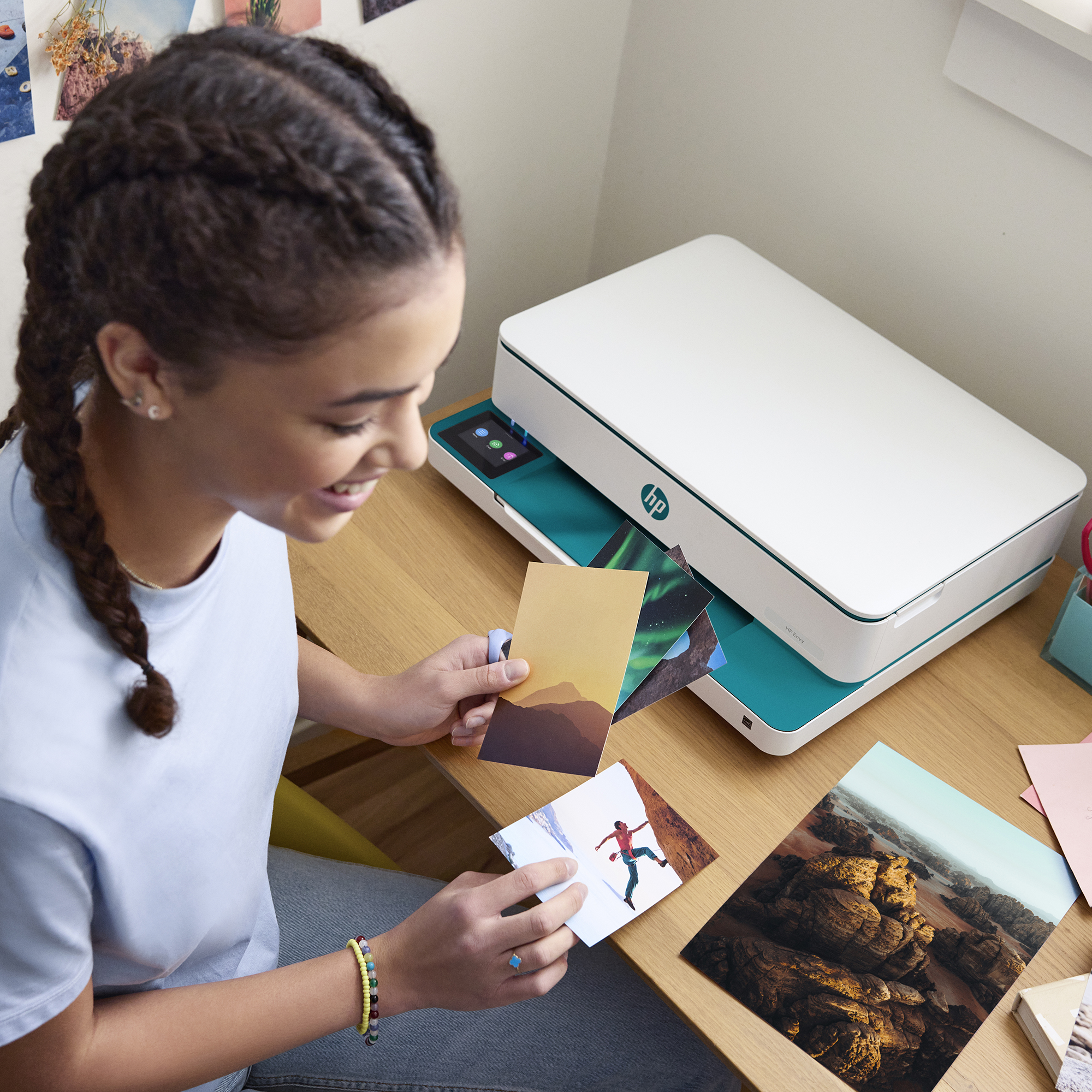 Dziewczyna z warkoczami trzyma zdjęcia przed drukarką. Uśmiecha się.