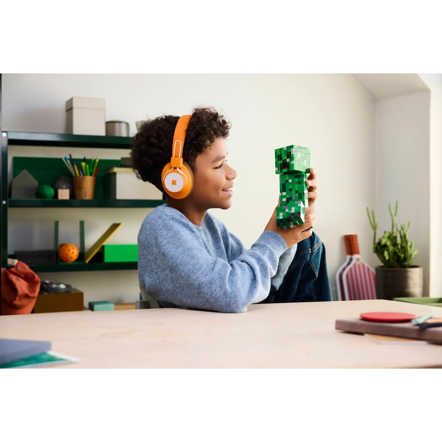A boy wearing orange headphones holds a green Minecraft figure.