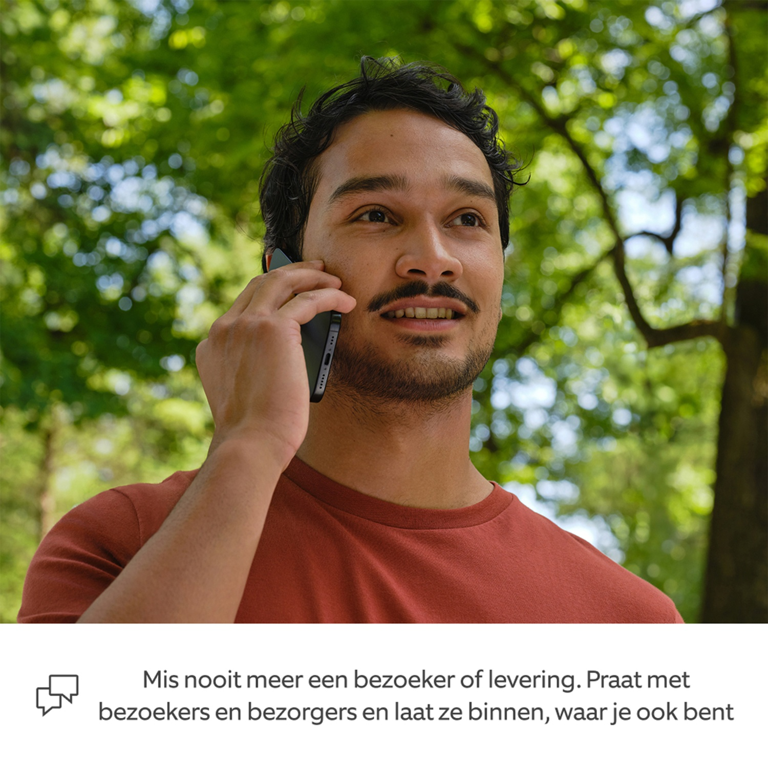 Homme parlant au téléphone en extérieur, avec des arbres verts en arrière-plan.