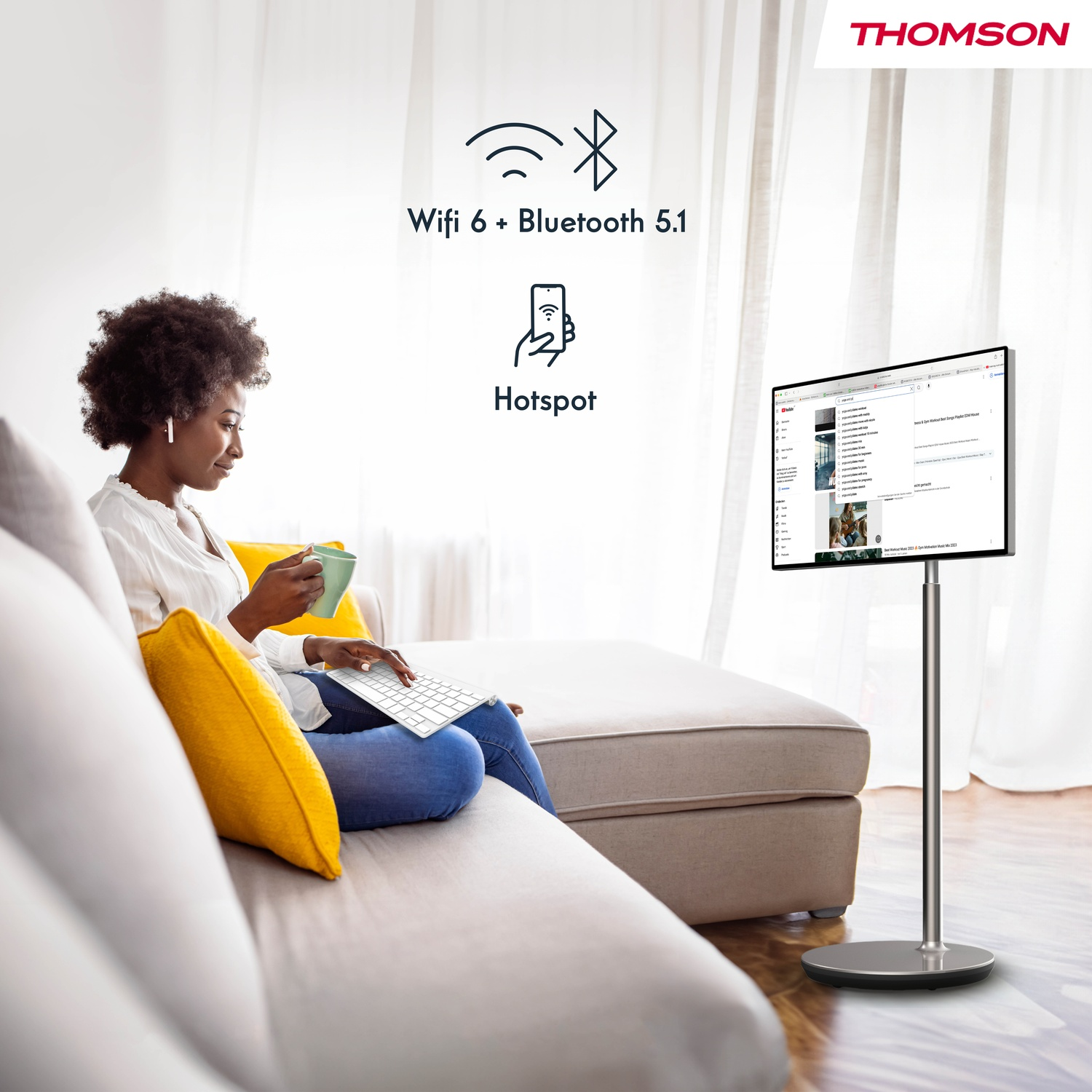 Donna su divano usa laptop. Una TV su supporto è accanto. Wifi 6, Bluetooth 5.1.