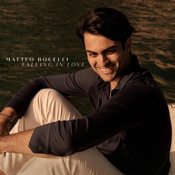 Matteo Bocelli sitzt auf einem Boot, lächelt und trägt ein dunkelblaues Hemd und weiße Hosen.