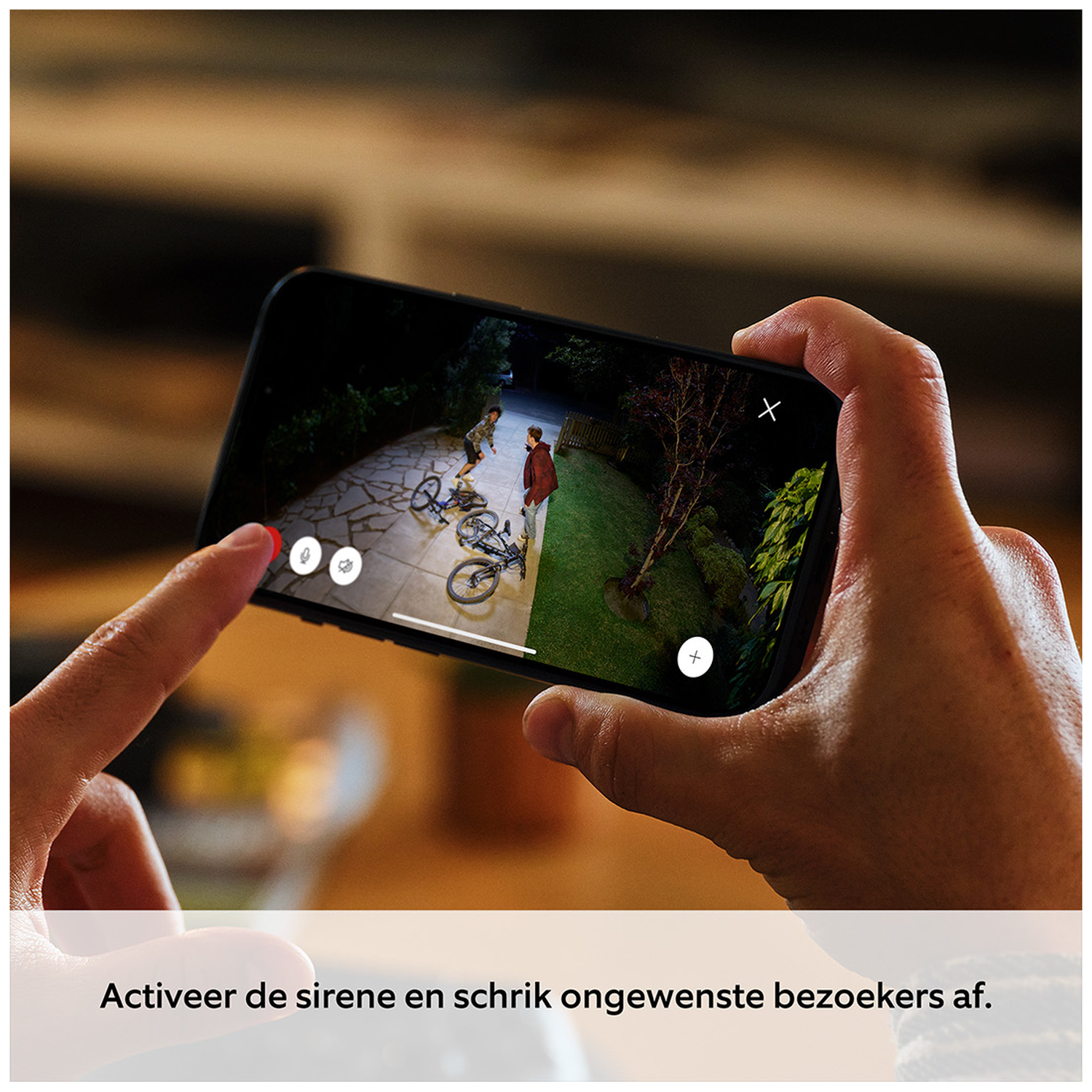 A hand holds a smartphone showing a security camera view of two people and bikes.
