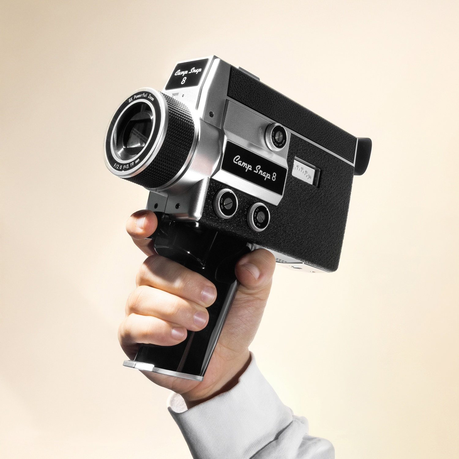 A hand holds a silver and black "Camp Snap 8" camera with a zoom lens.
