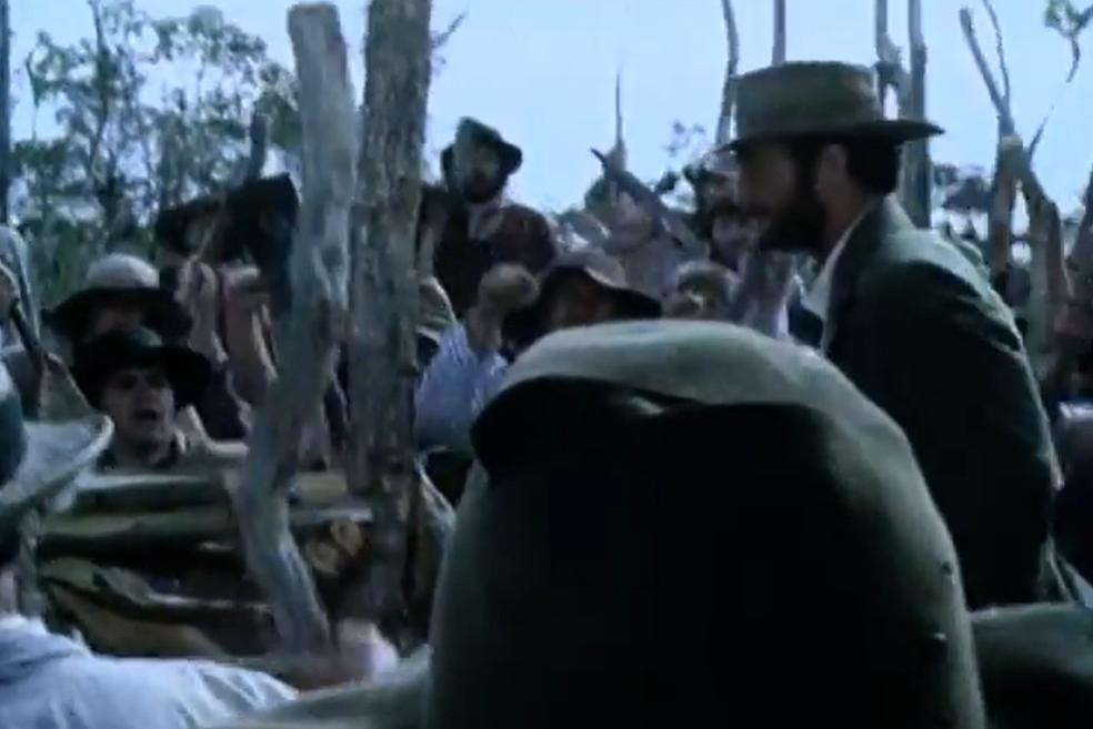 Eine Gruppe von Männern in Hüten versammelt sich im Freien, einige schauen nach rechts.