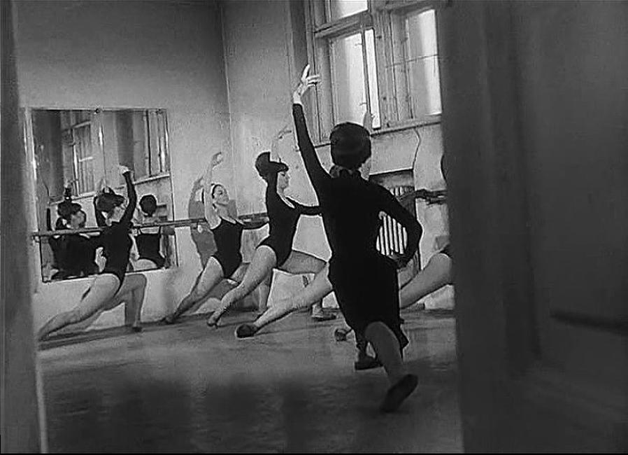 Balletttänzerinnen üben vor einem Spiegel an einer Ballettstange in einem Raum.