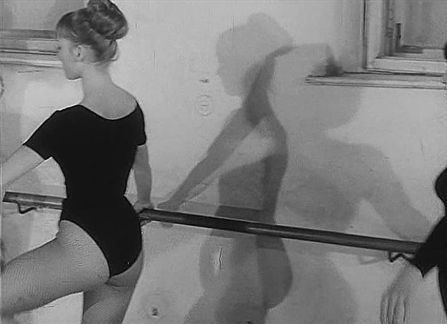 Tänzerin im schwarzen Trikot hält sich am Ballettstange fest, Schatten an Wand.