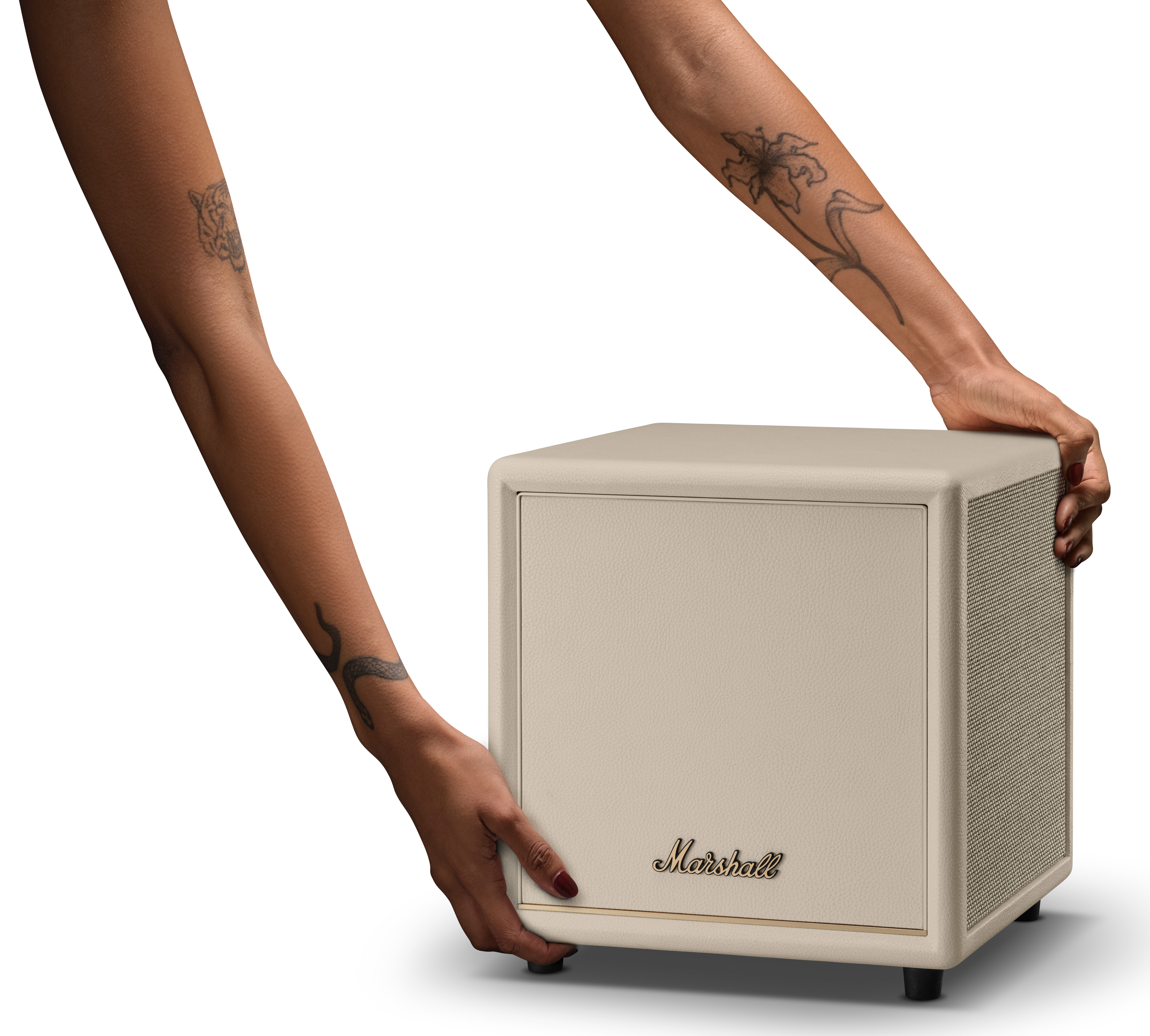 Osoba z tatuażami sięga po beżowy głośnik Marshall.