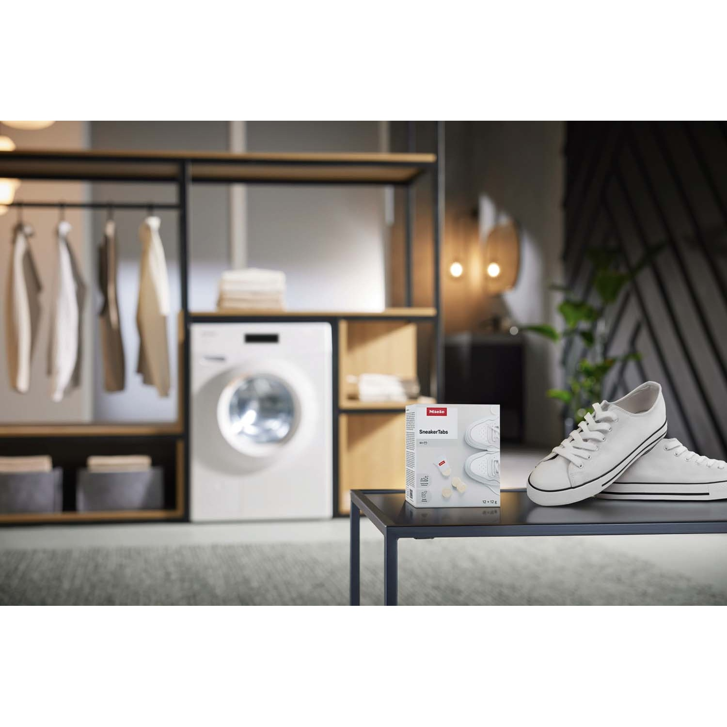 Sneakers bianche e scatola SneakerTabs su tavolo. Lavatrice e vestiti sullo sfondo.